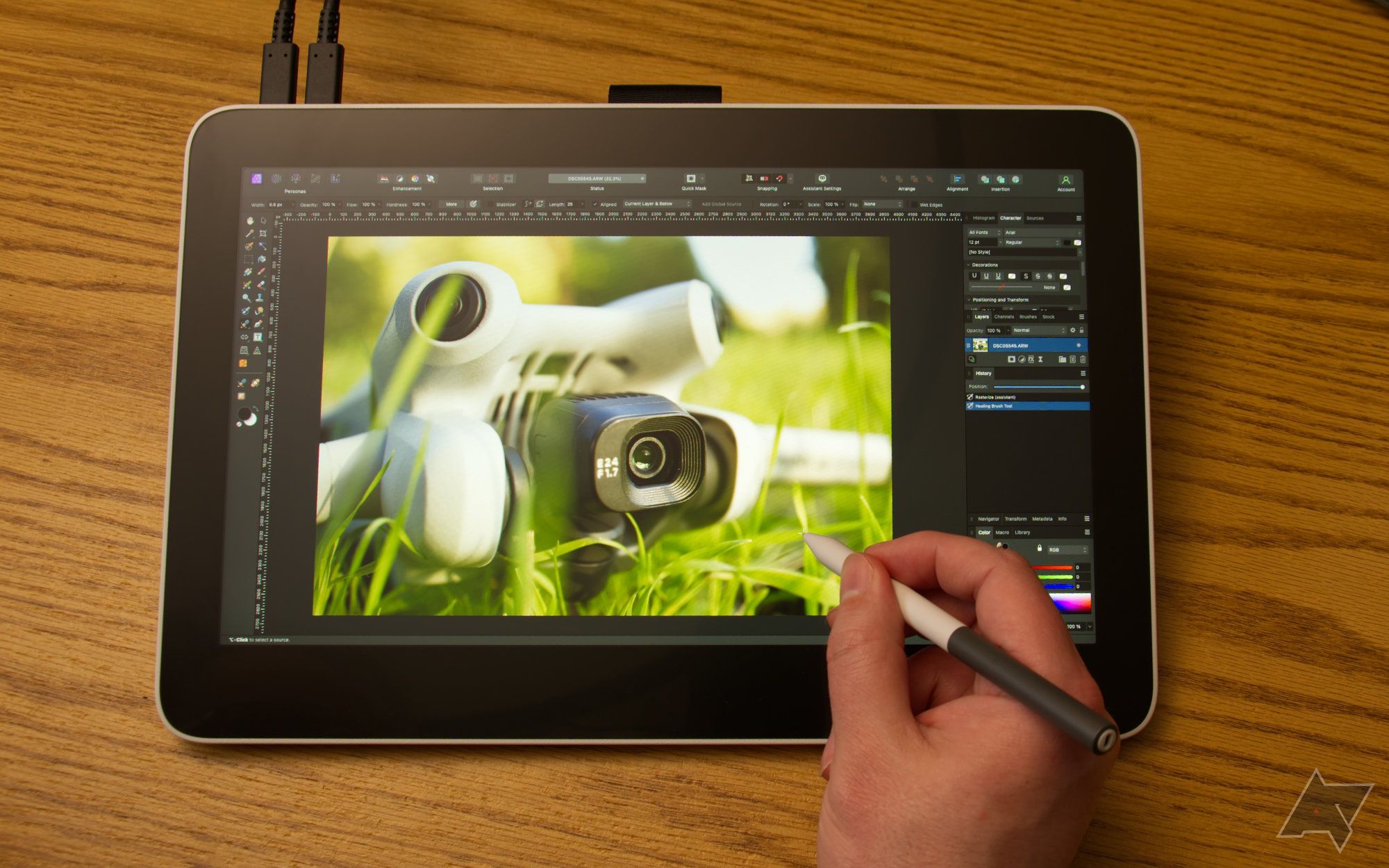 Wacom One 13 Touch deitado sobre uma mesa com uma mão segurando uma caneta, usada para editar a imagem de uma câmera drone