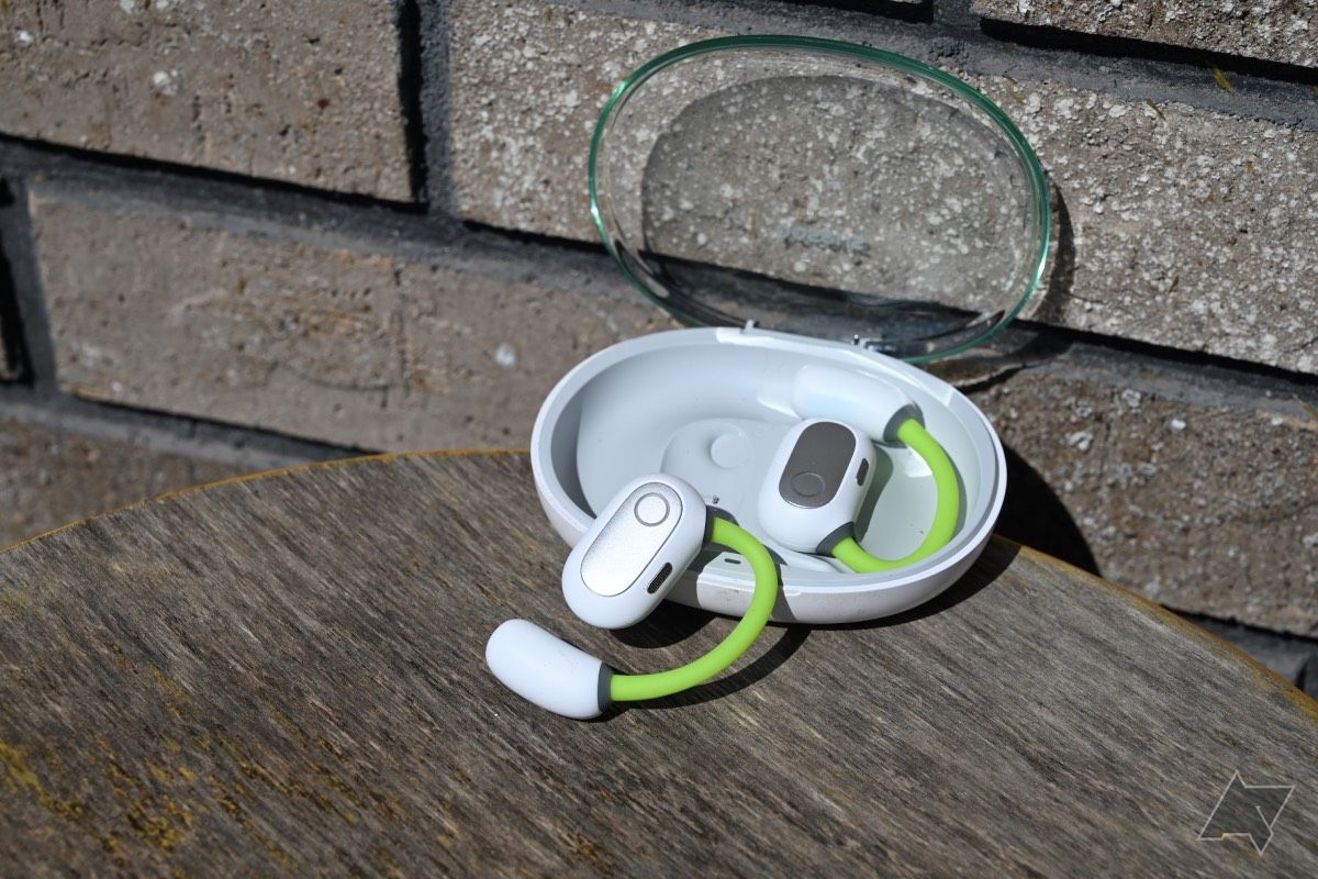 Foto lateral dos fones de ouvido Baseus Eli Sport 1 Open-Ear TWS branco e verde neon em fundo de tijolo com um botão no estojo de carregamento.