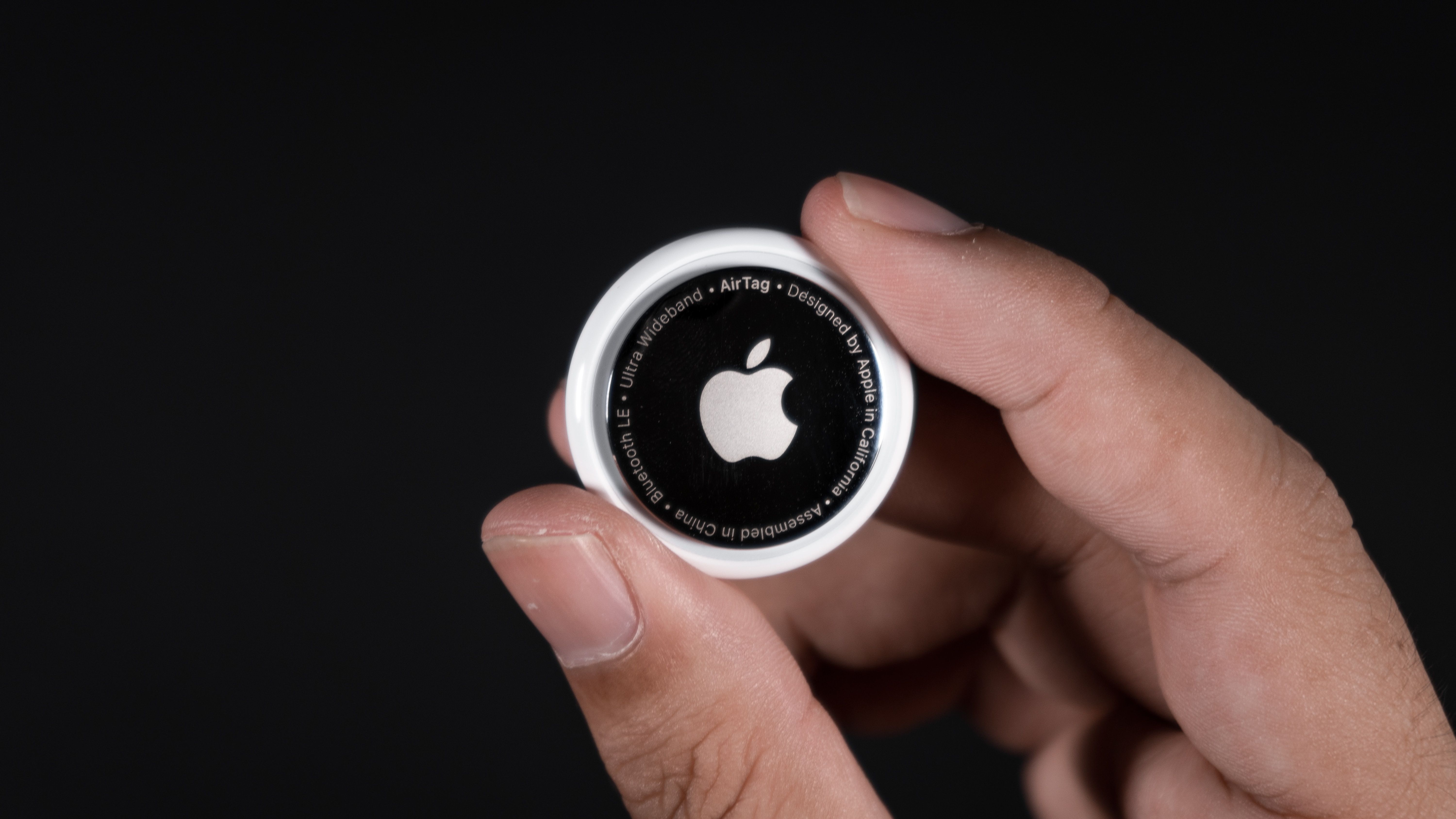 Foto aproximada de um Apple AirTag nas mãos contra um fundo preto