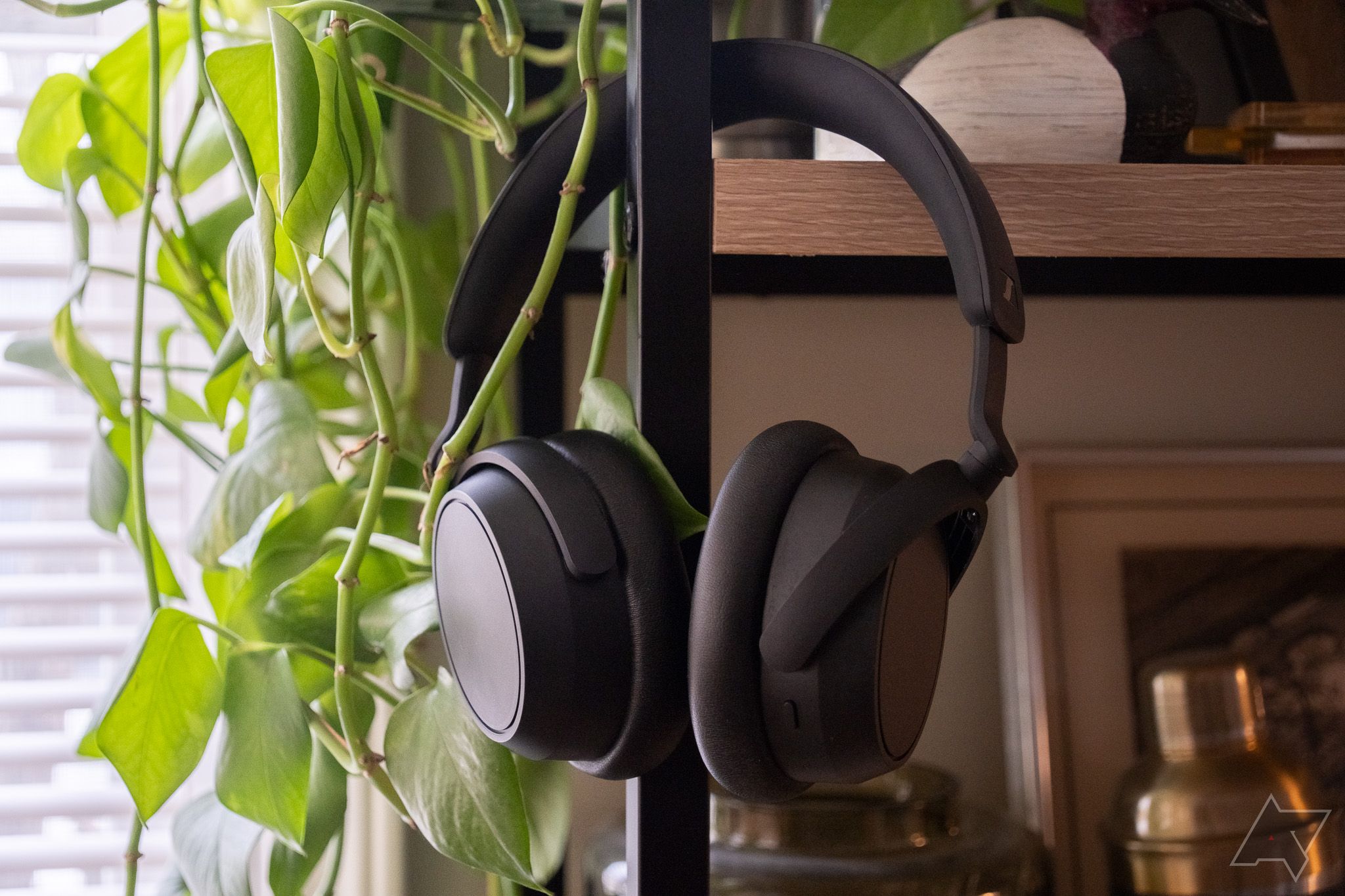 Um par de fones de ouvido pretos pendurados em uma prateleira ao lado de uma planta