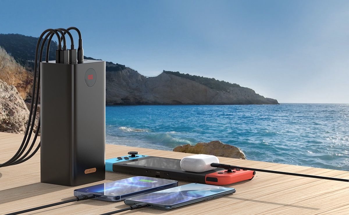 Carregador portátil de alta capacidade Romoss sentado na praia, carregando um Nintendo Switch, AirPods e dois telefones Android