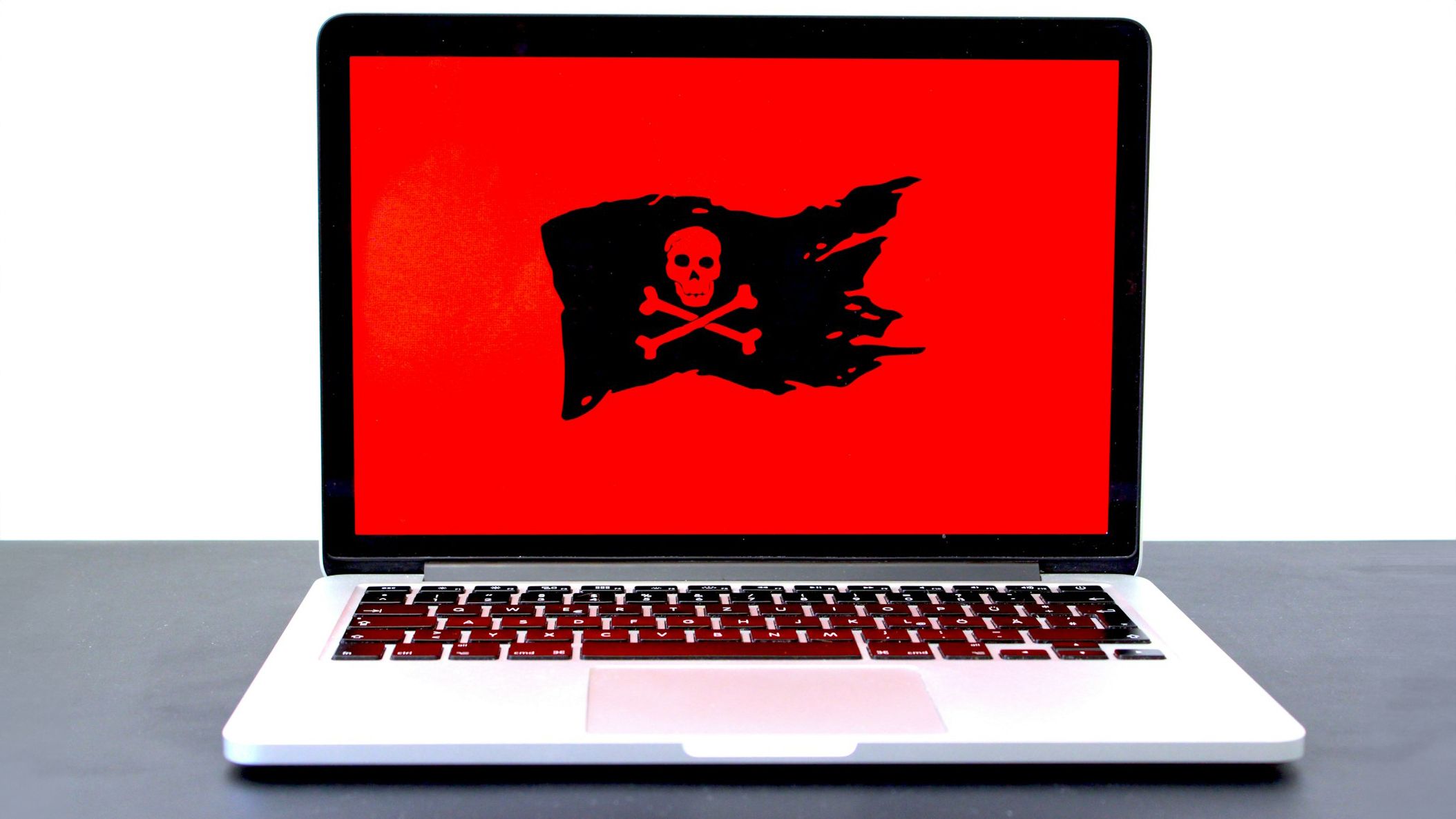 Um laptop sobre uma mesa exibindo uma grande tela vermelha com um símbolo de bandeira pirata preta, indicando uma possível ameaça de ransomware ou segurança cibernética.