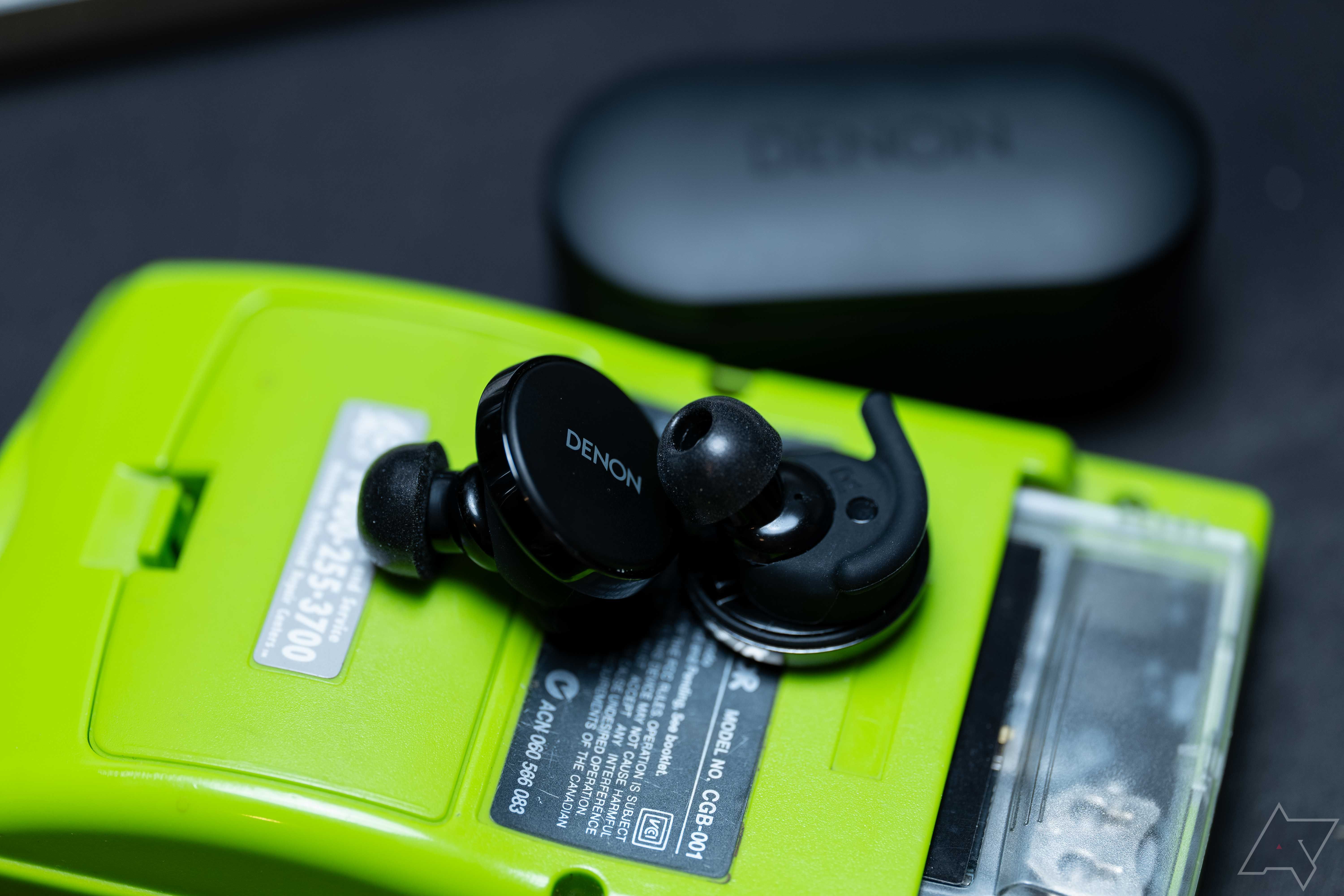 Os fones de ouvido Denon PerL Pro colocados na parte de trás de um Gameboy Color verde limão, com asas grandes e pontas de espuma nos fones de ouvido