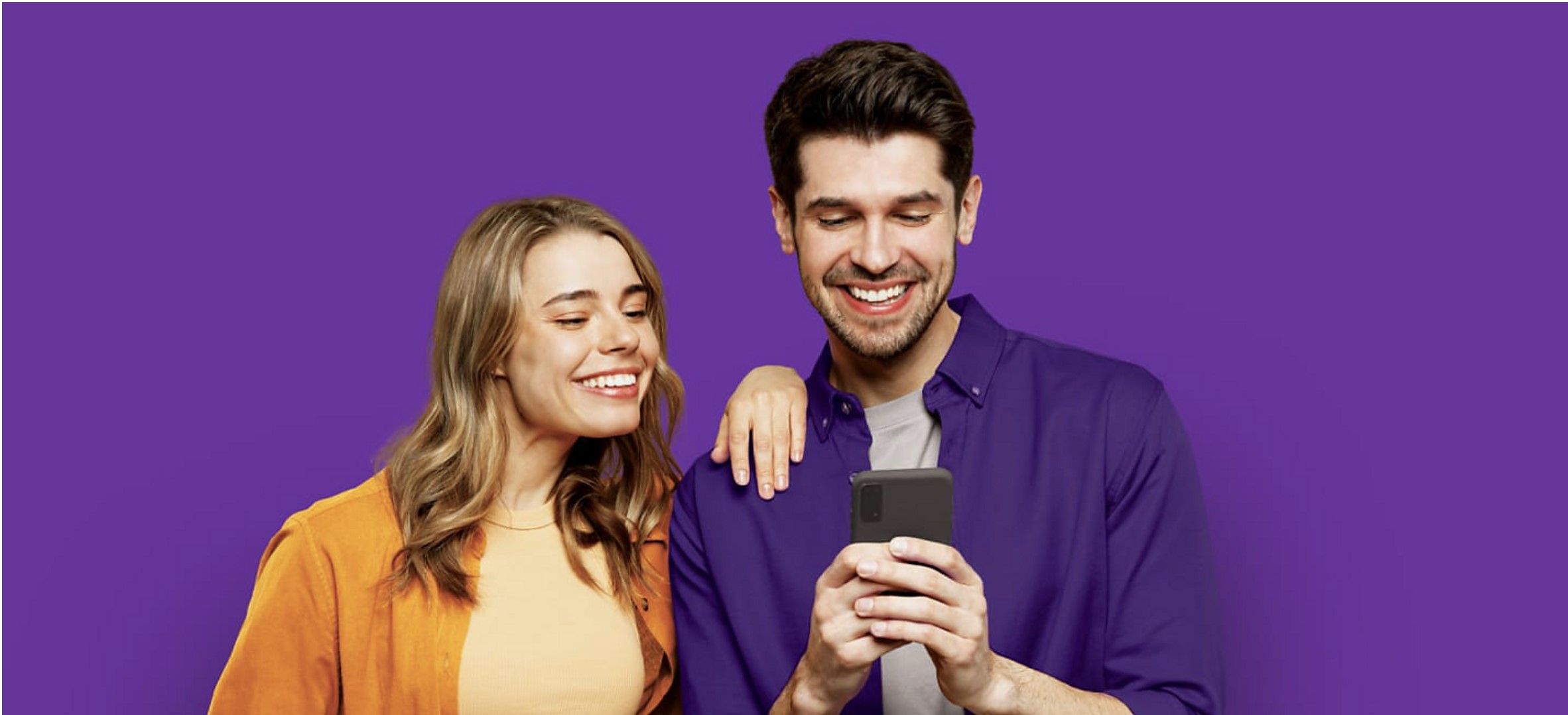 Duas pessoas sorrindo e segurando telefones enquanto olham para um dos telefones das pessoas
