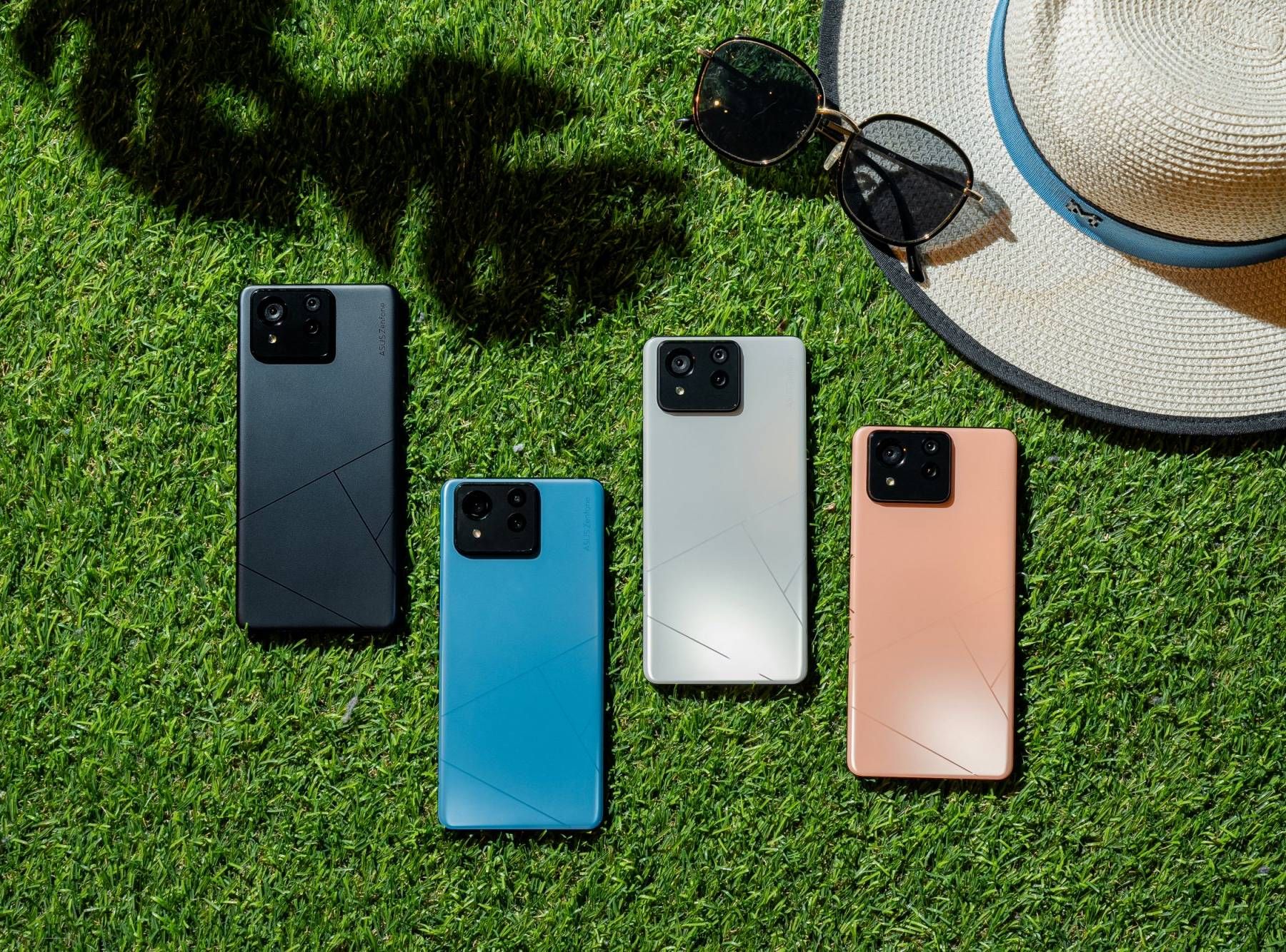 Quatro cores diferentes do Asus Zenfone 11 Ultra sentado de bruços na grama perto de um chapéu de sol e óculos de sol