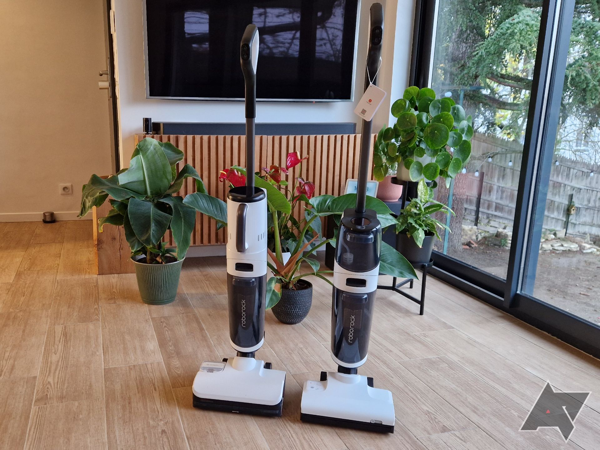 Imagem do Roborock Dyad Pro Combo e Dyad Air (à direita) um ao lado do outro, com plantas e uma TV ao fundo