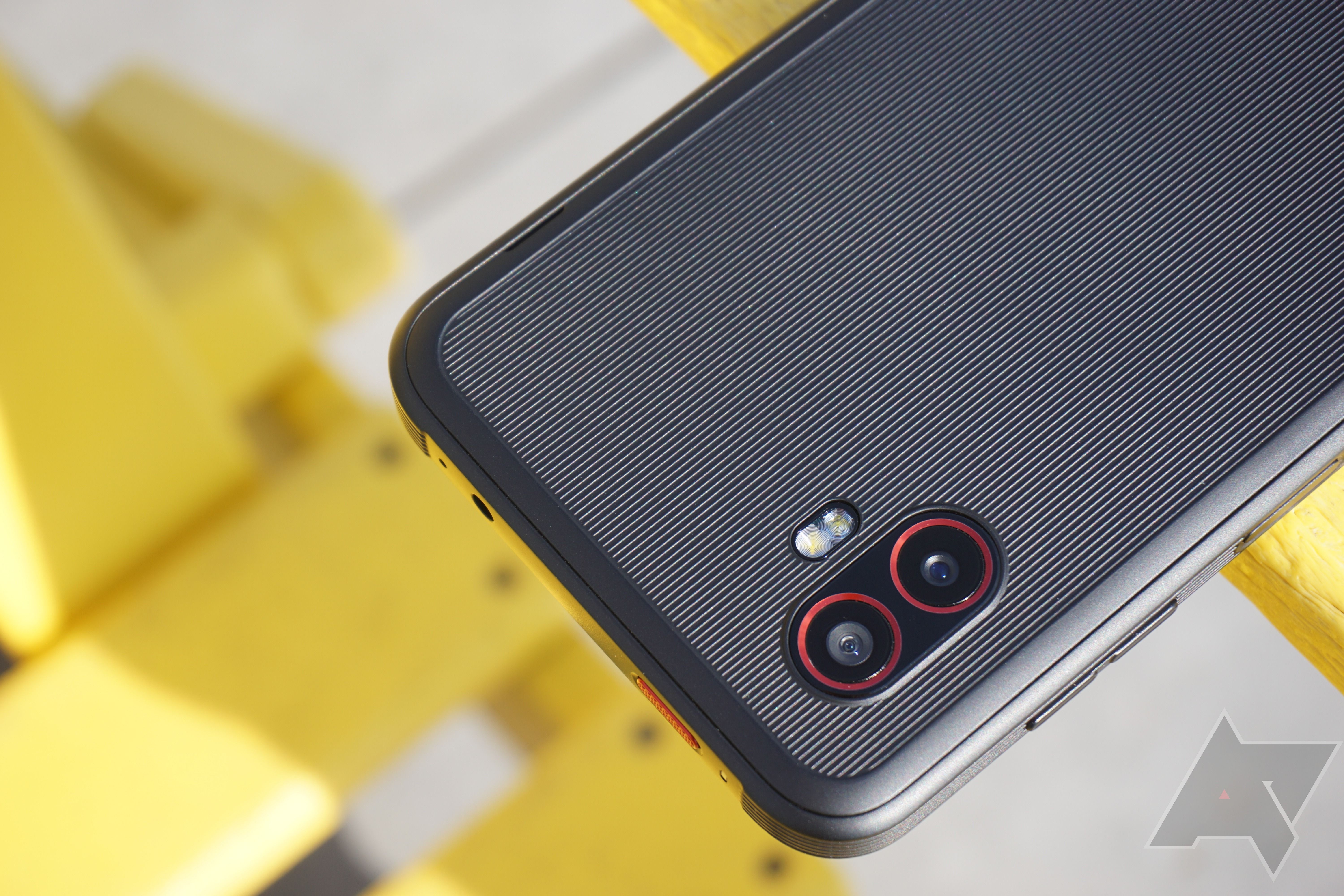 Uma imagem da parte superior do Samsung XCover6 Pro mostrando os módulos da câmera com um banco de ripas amarelo ao fundo.