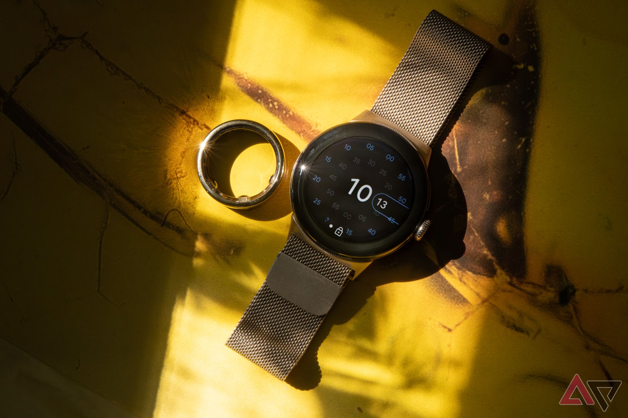 Um anel inteligente ao lado de um smartwatch em um fundo amarelo