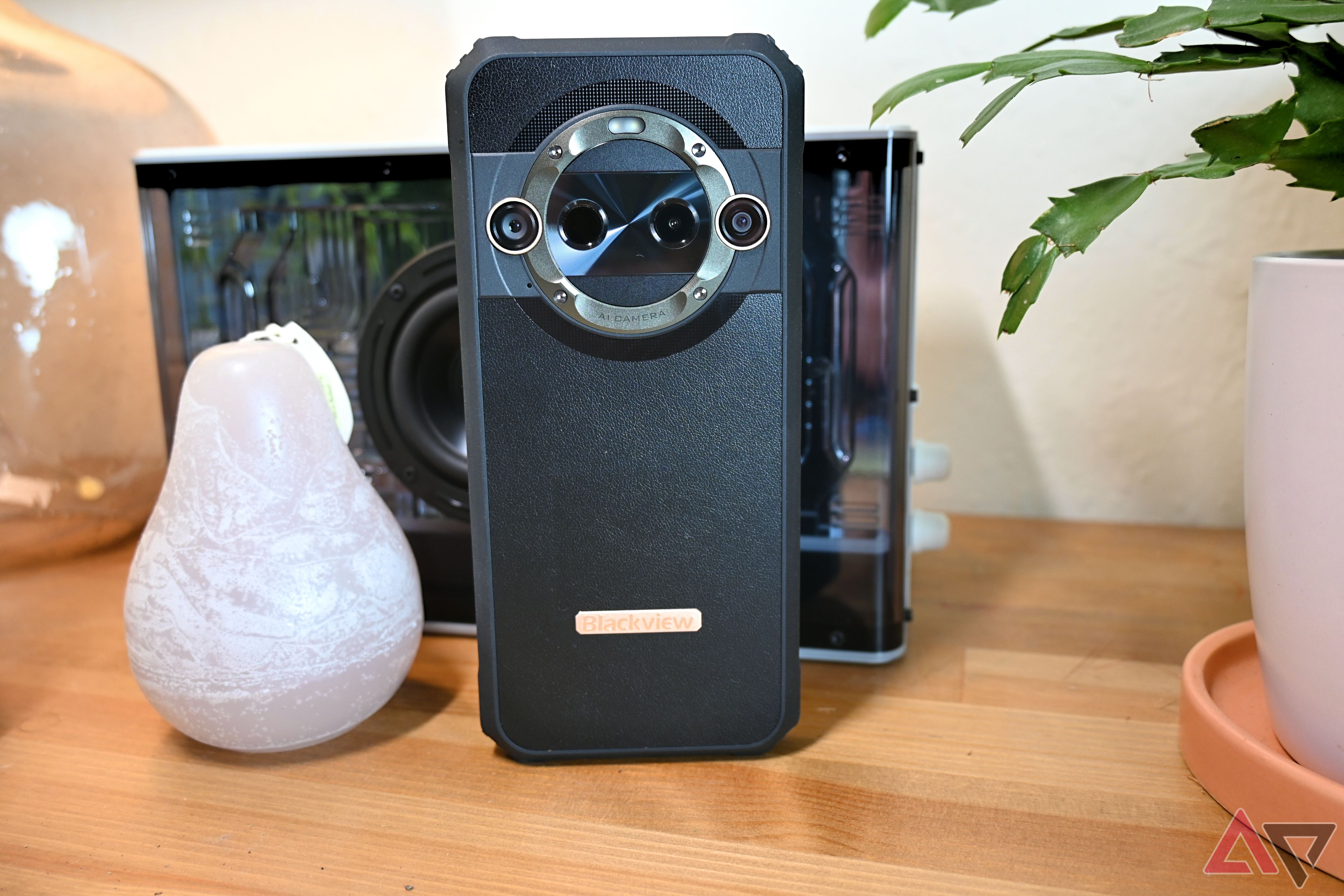 Blackview BL9000 Pro em preto sobre uma mesa de madeira clara em frente a um alto-falante e ao lado de uma vela.