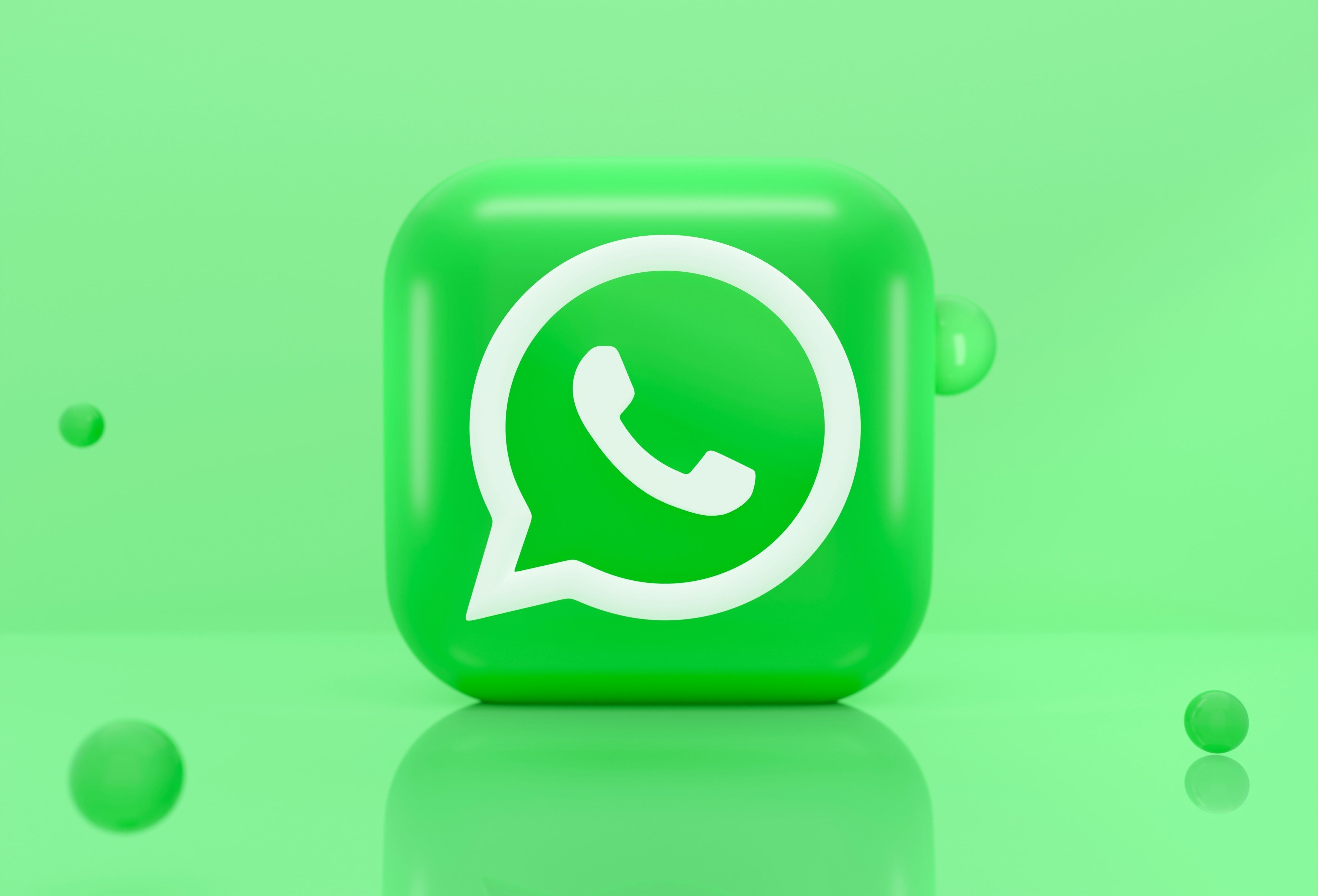 O logotipo frontal do WhatsApp é exibido em um cubo verde tridimensional sobre um fundo verde sólido.  Bolhas verdes escuras adicionam interesse visual à imagem.
