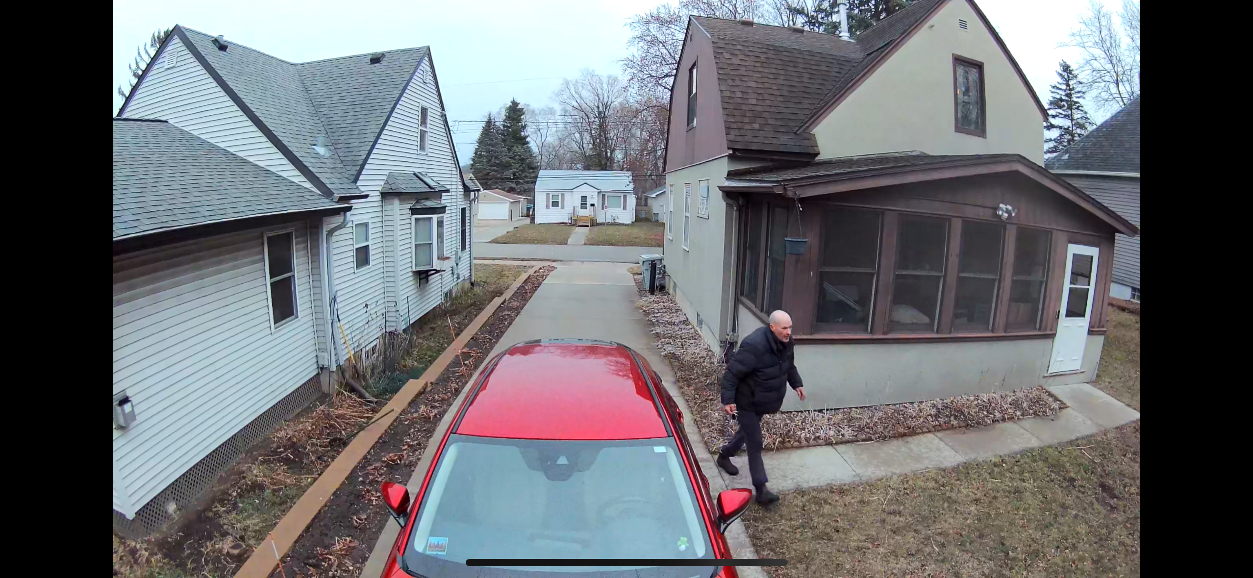 Homem atravessando a garagem perto de casa e carro vermelho