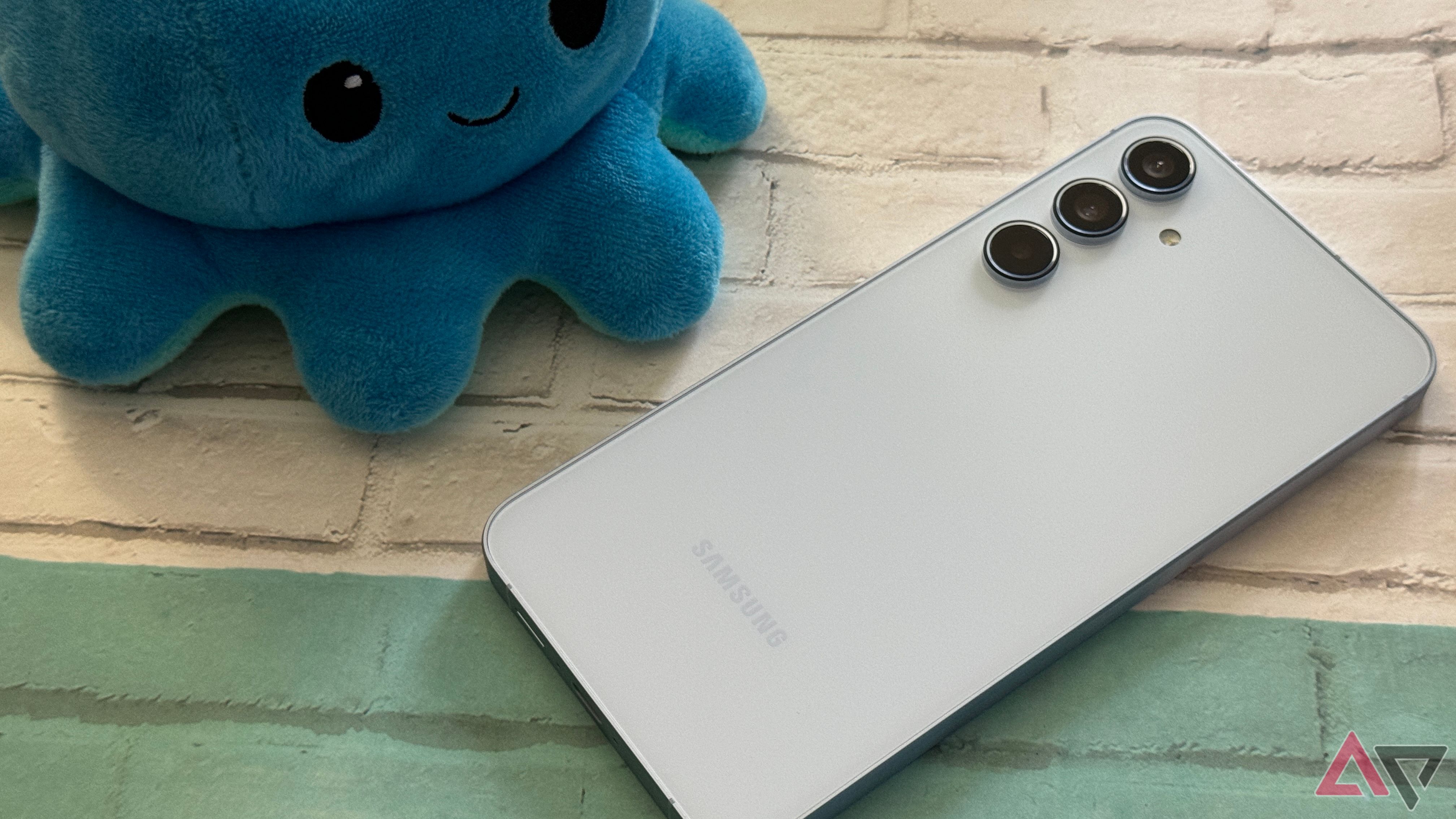 Samsung Galaxy A55 em azul deitado contra um fundo com um pelúcia