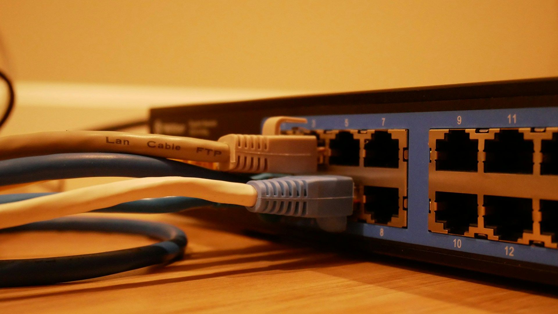 A imagem mostra um close de um switch de rede com cabos Ethernet conectados em algumas portas, rotulados com números, indicando uma configuração para rede local.
