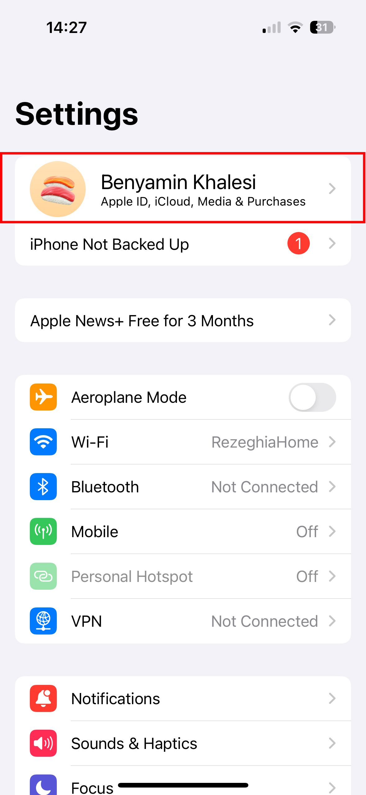 Uma captura de tela do menu de configurações do iPhone mostrando os detalhes do ID Apple do usuário na parte superior, junto com outras configurações como Modo Avião, Wi-Fi e Bluetooth.