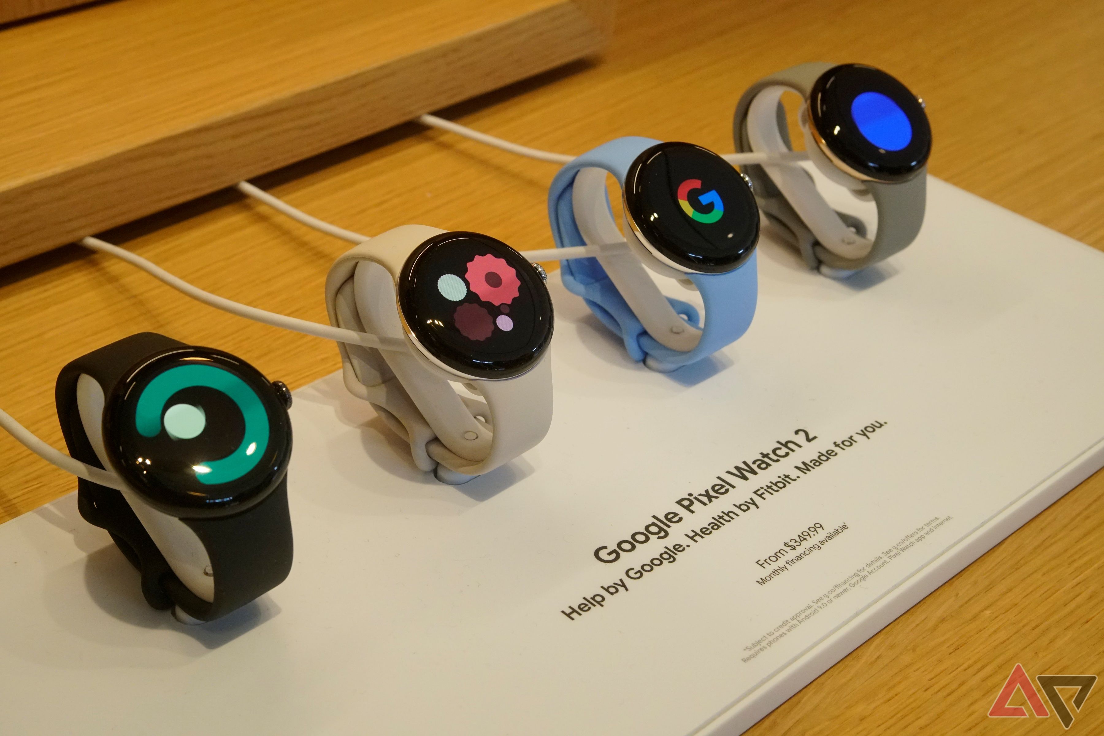 Quatro unidades do Google Pixel Watch 2 carregando em uma mesa de varejo.