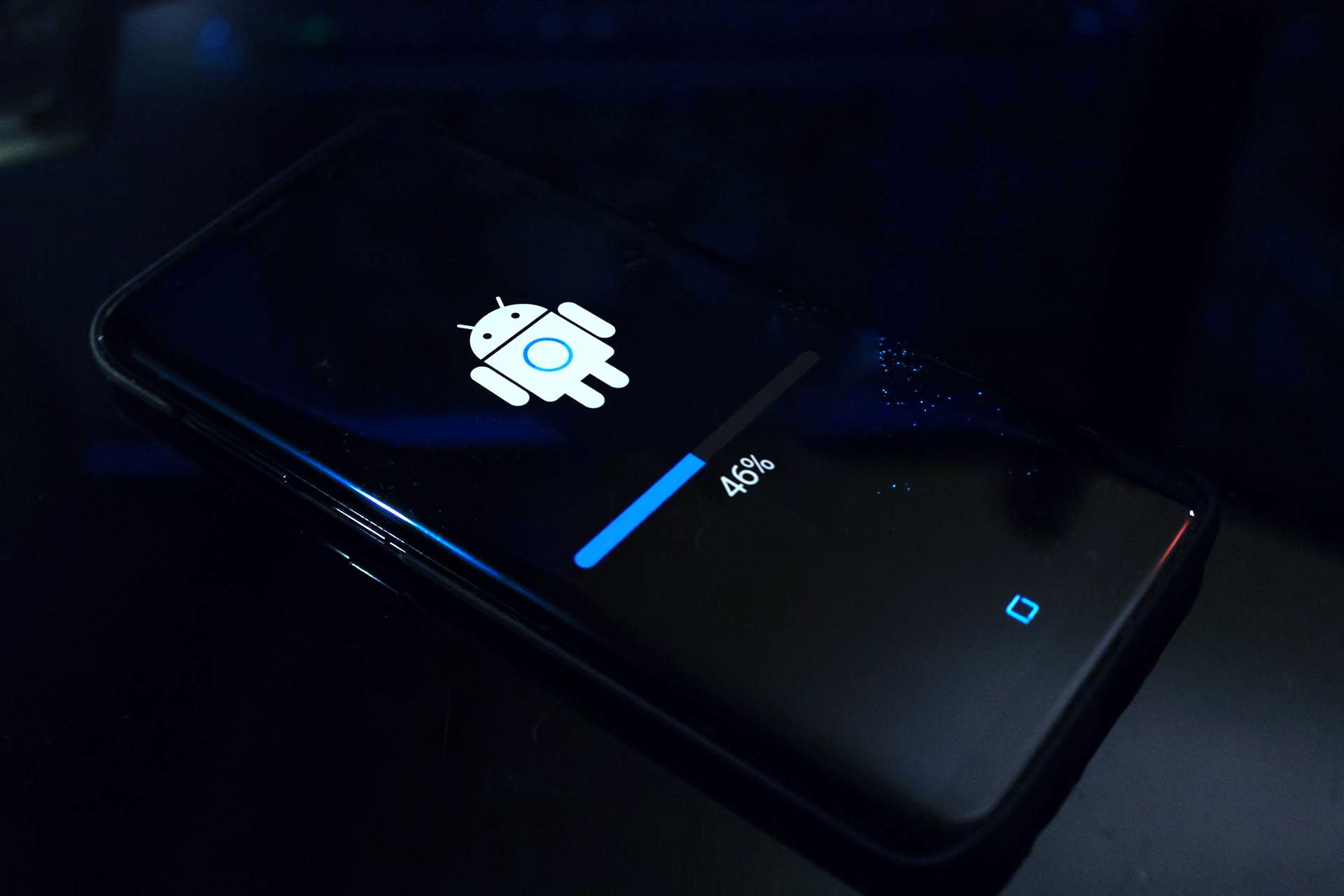 Um smartphone Android apoiado em uma superfície exibindo uma tela de atualização com um ícone de robô Android e uma barra de progresso indicando 46% de conclusão.