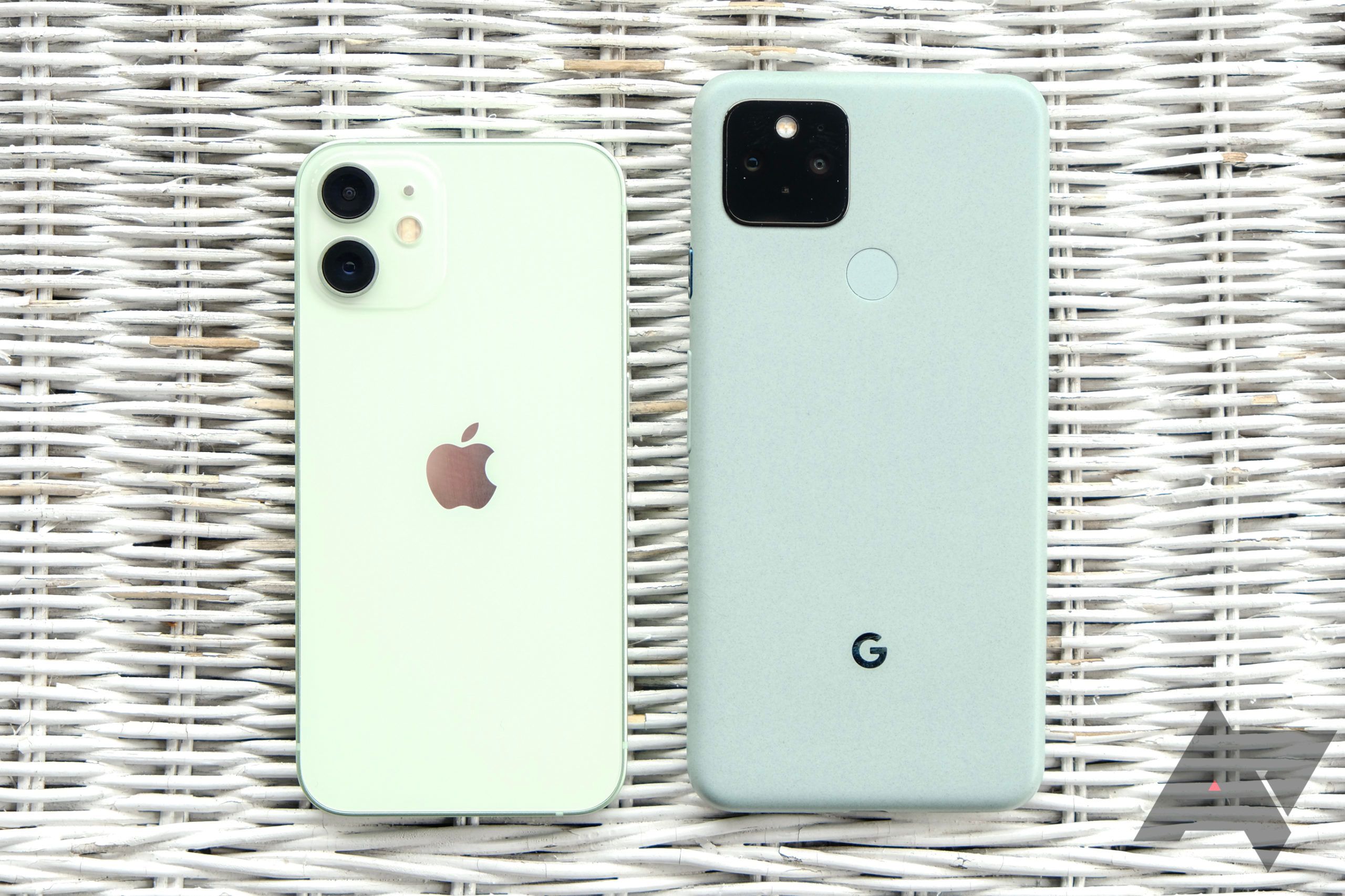 Um iPhone 12 Mini ao lado de um Pixel 5 em um cenário de vime branco
