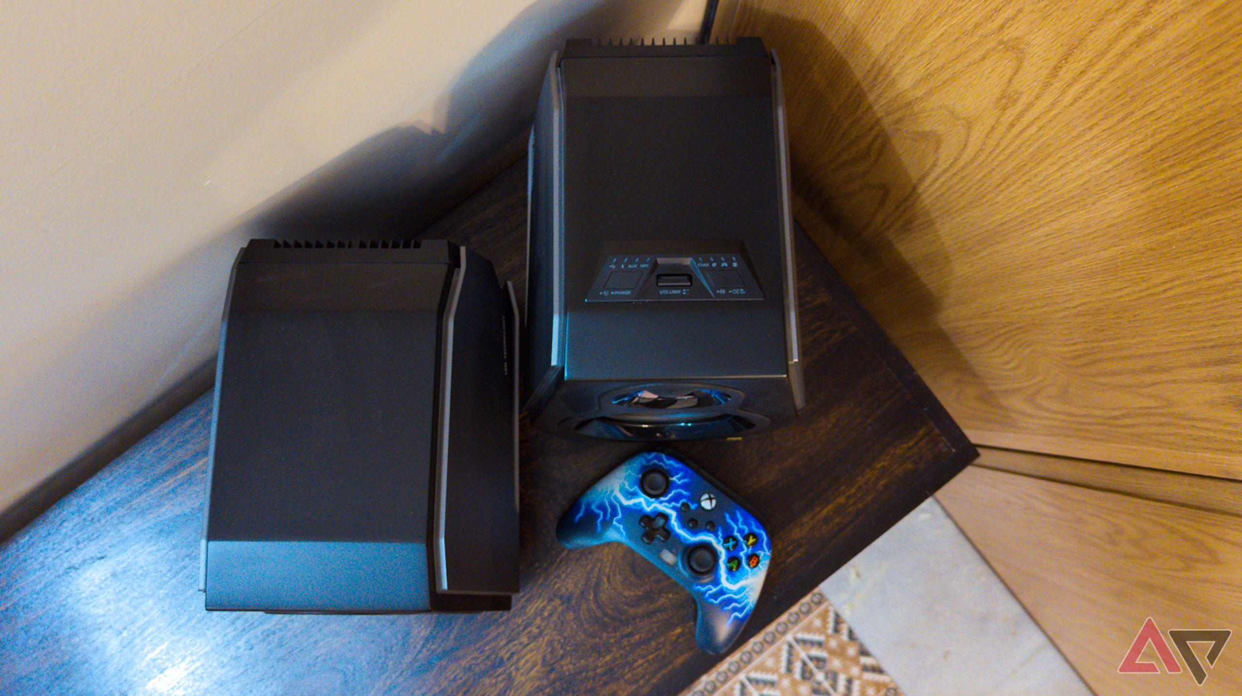 Imagem de cima para baixo dos alto-falantes Hecate G5000 com um controlador de jogo em uma prateleira de madeira de nogueira escura