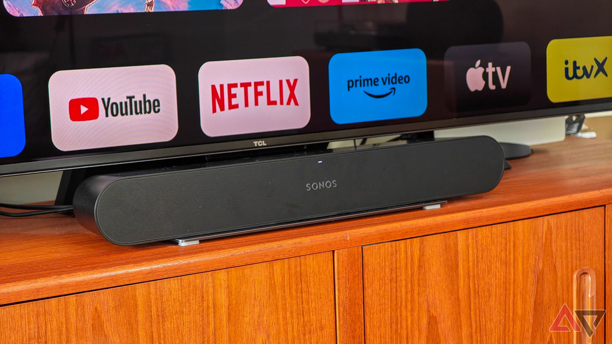 Sonos Ray em um aparador de madeira sob uma TV mostrando logotipos de aplicativos de streaming