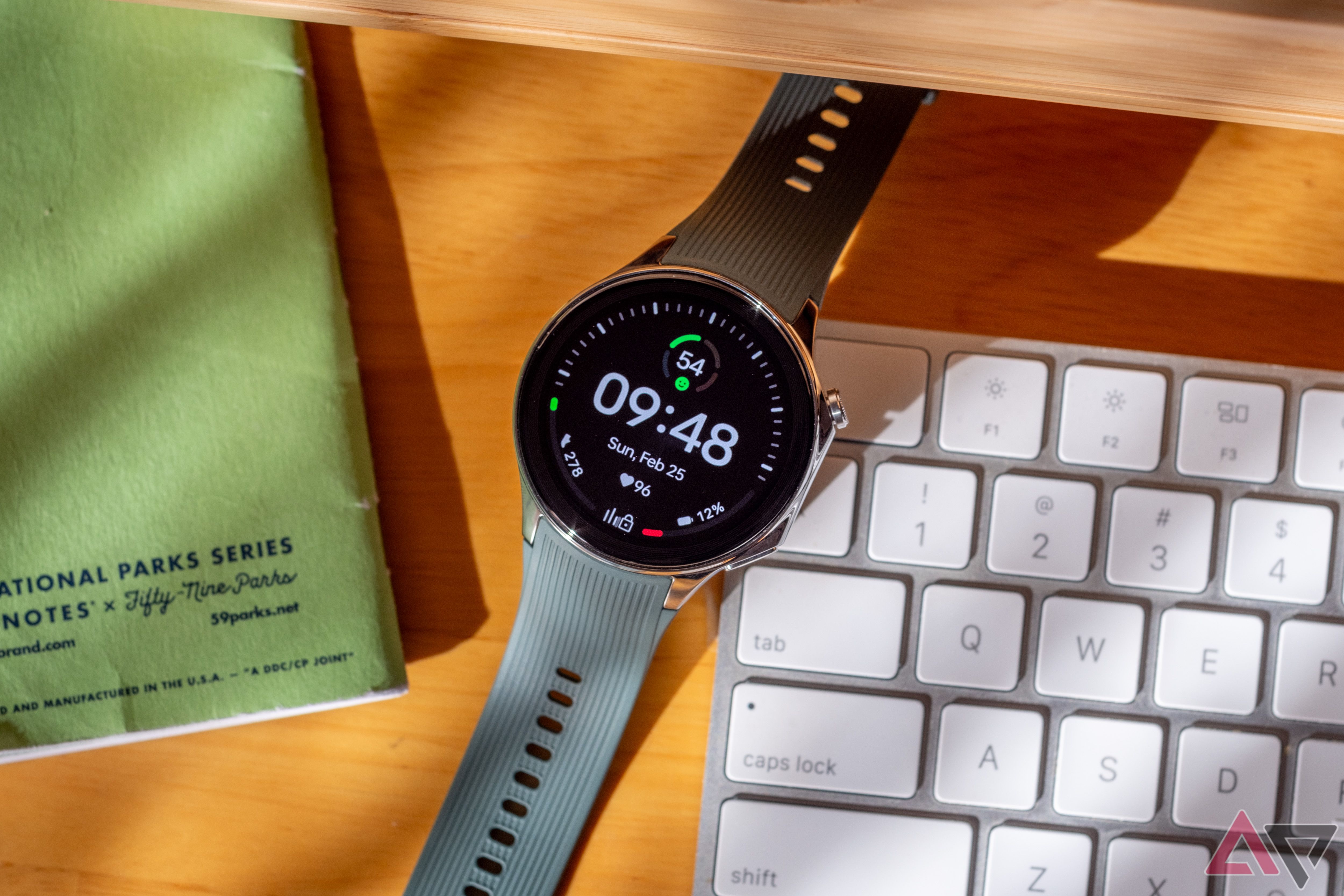 Um smartwatch em uma mesa entre um notebook e um teclado