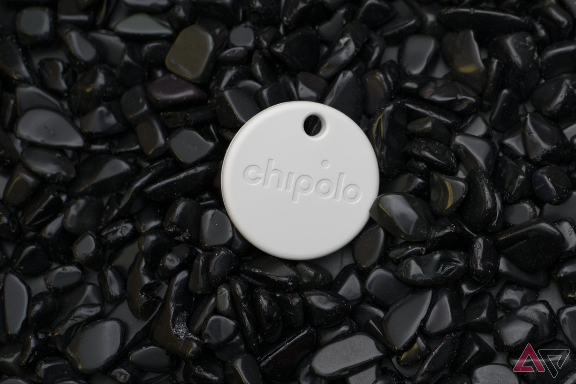 Etiqueta Chipolo One Point apoiada em uma cama de pedras de obsidiana
