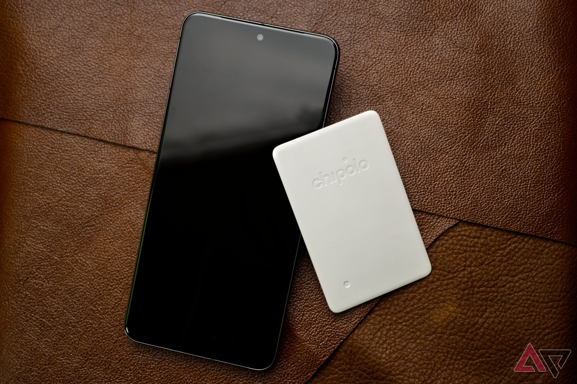 Chipolo CARD Point e um smartphone apoiado em folhas de couro marrom