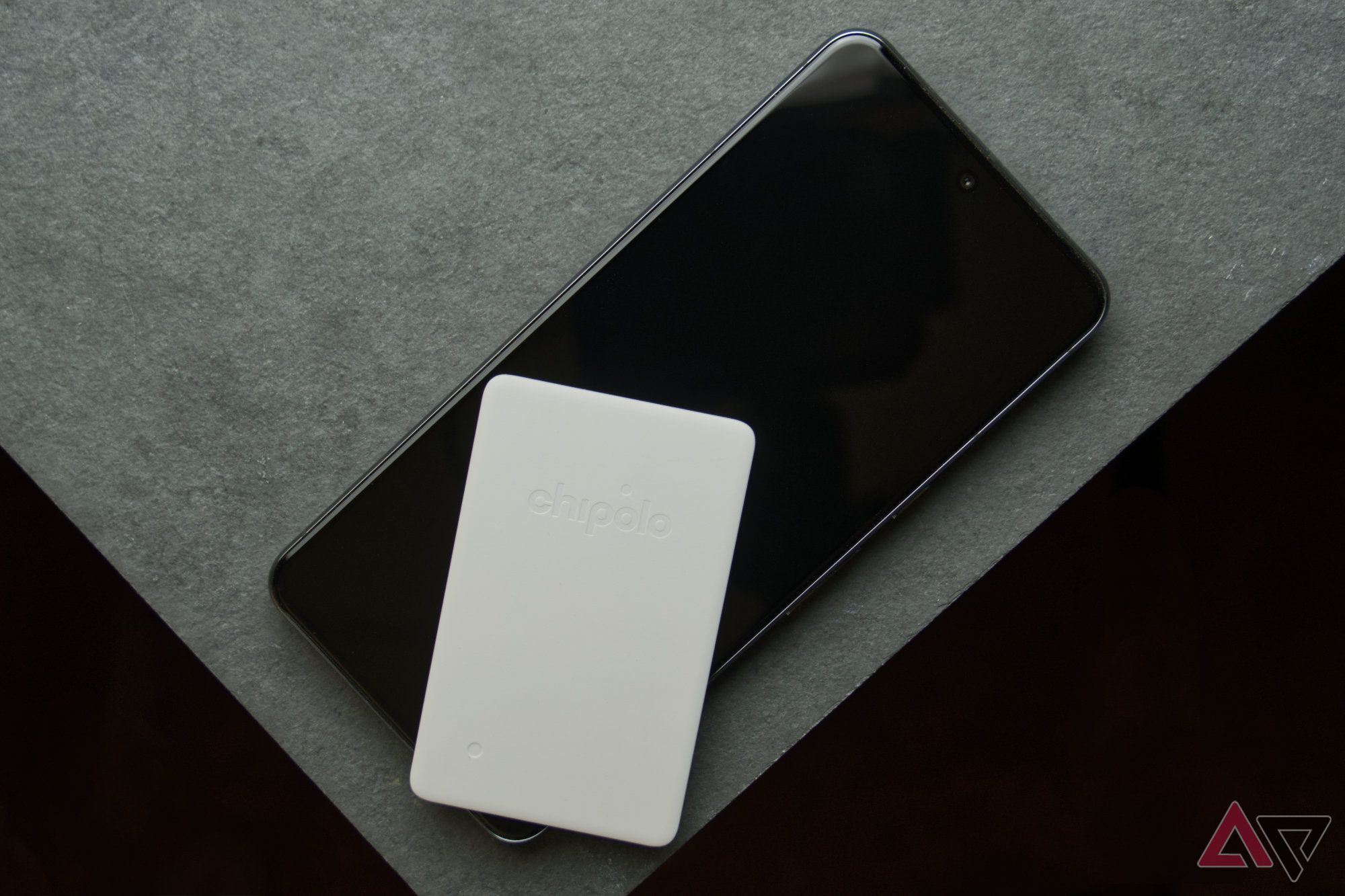 Chipolo CARD Point em um smartphone apoiado em um ladrilho cinza