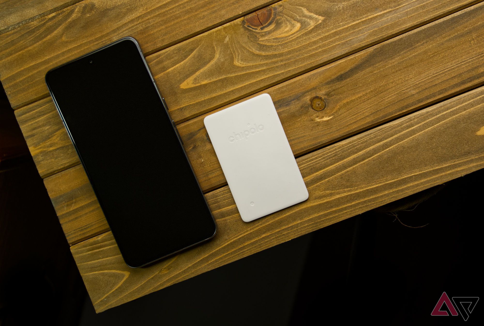 Chipolo CARD Point e um smartphone em uma prancha de madeira