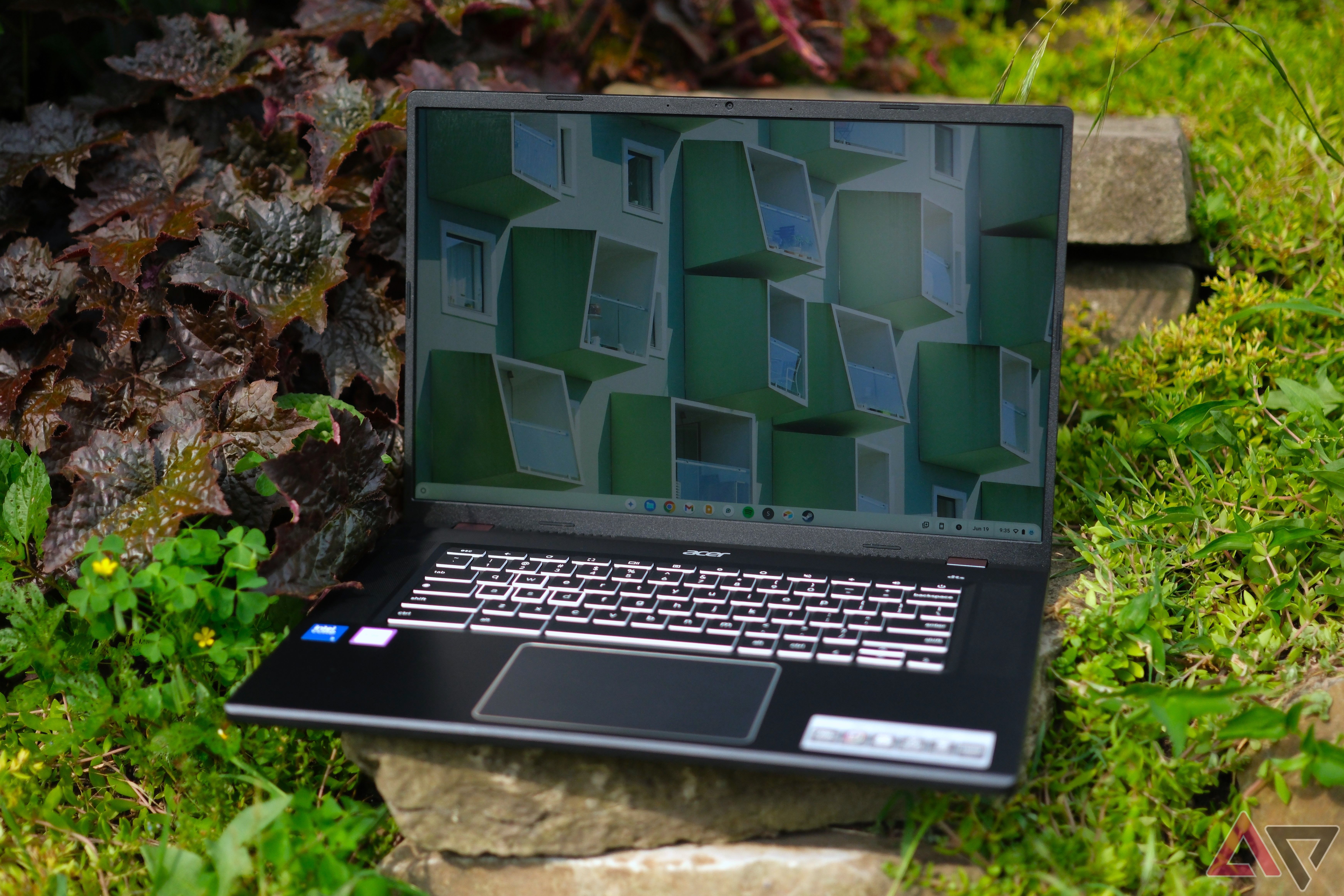 Acer Chromebook Plus 516 GE (2024) sentado em uma rocha com plantas ao redor, com a tampa aberta e a tela ligada