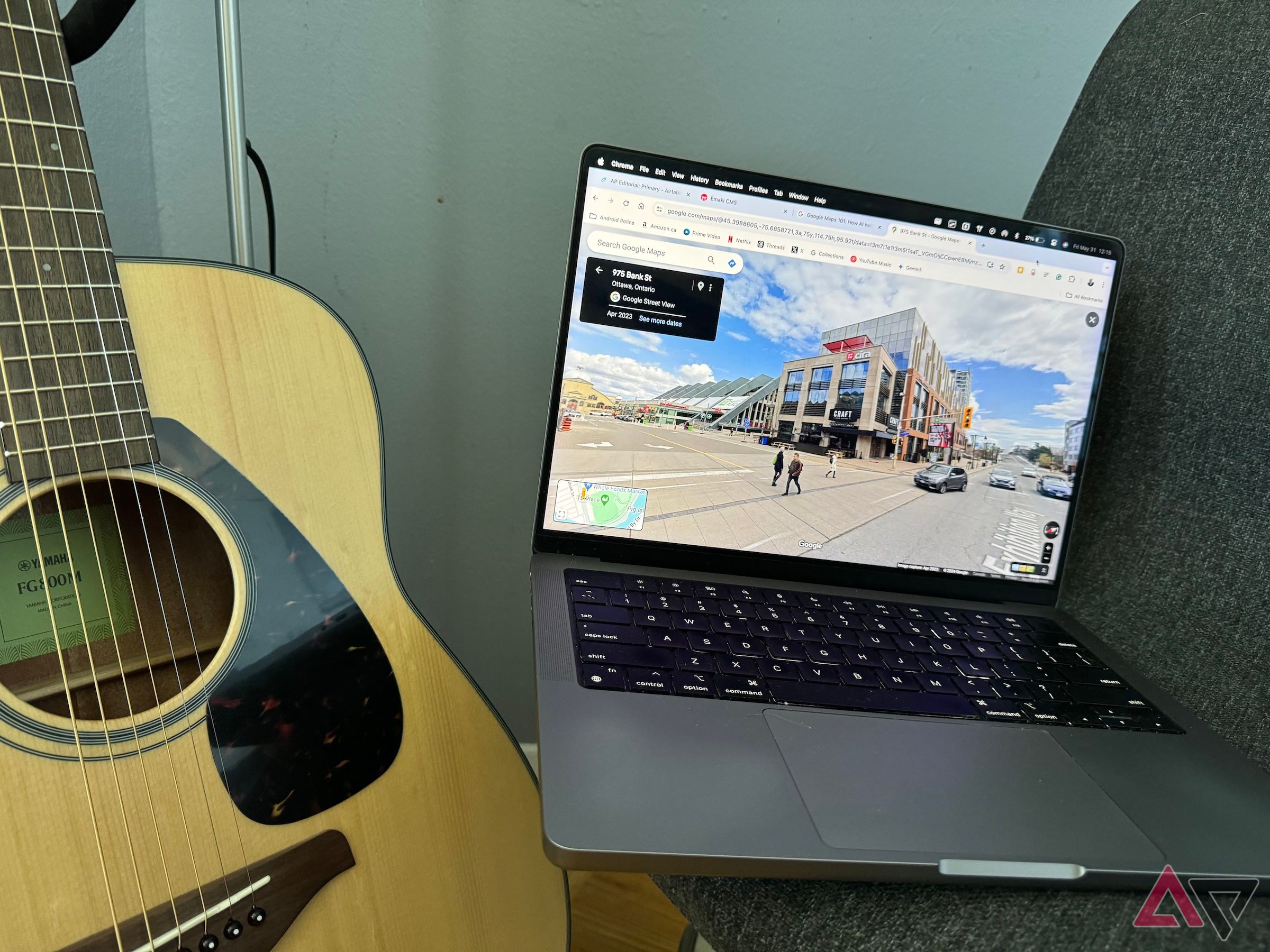 Streetview em um MacBook Pro sentado em uma cadeira cinza ao lado de um violão.