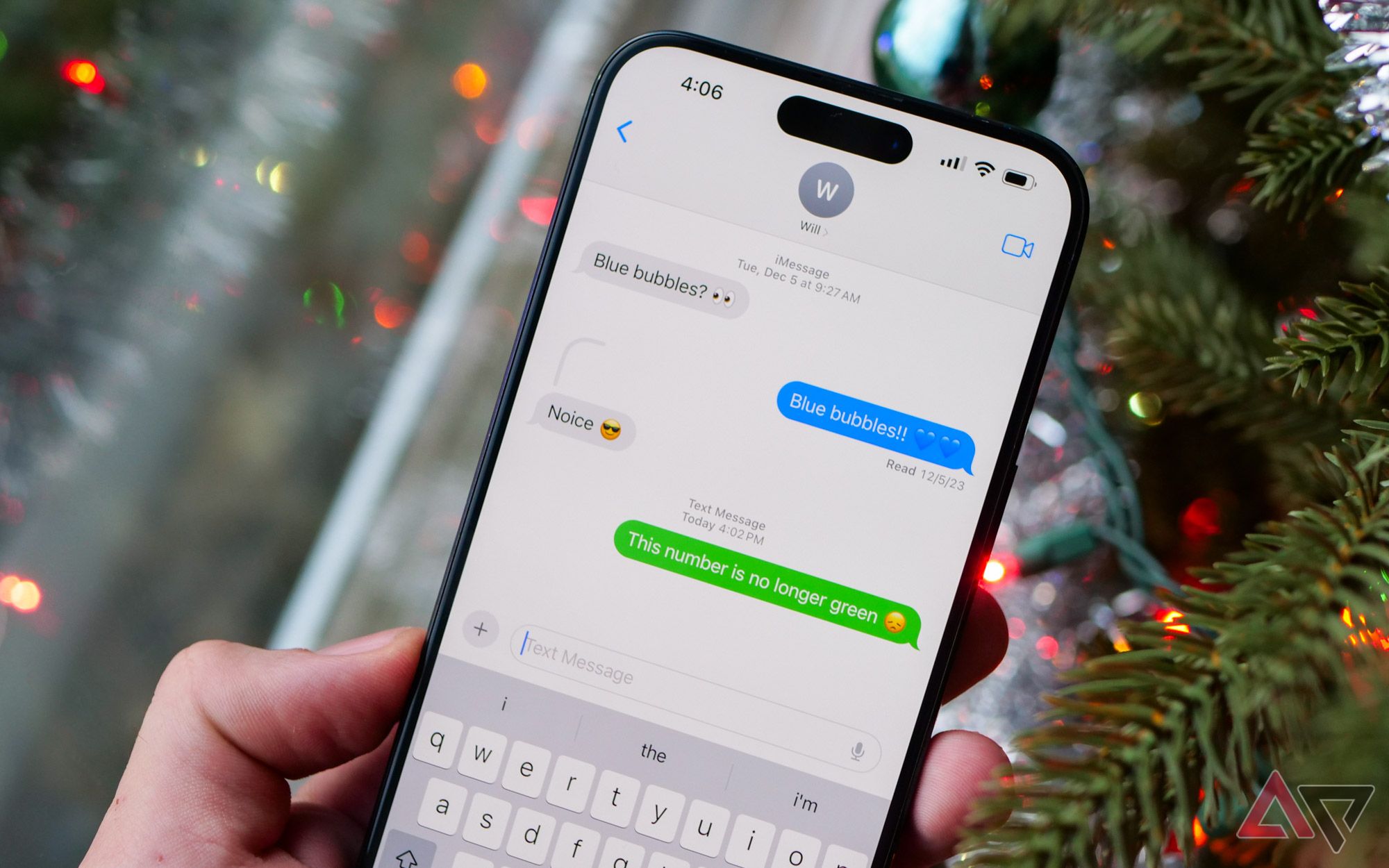 Um iPhone 15 Pro Max em frente a uma árvore de Natal com o Mensagens aberto.