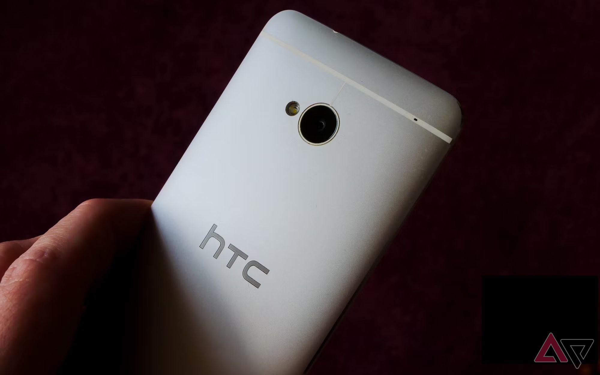 Uma mão segurando um HTC One M7 contra um fundo preto escuro.