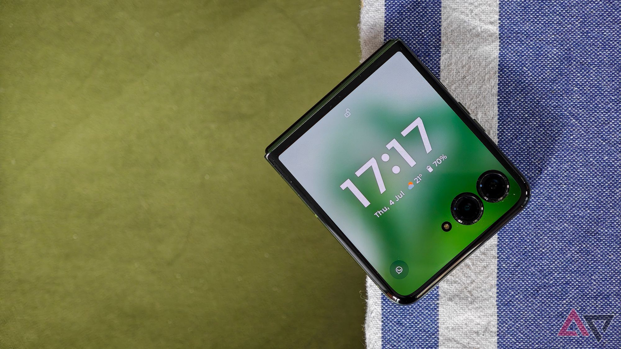 Motorola Razr+ mostrando as horas na tela de capa, apoiado em uma toalha de mesa azul sobre um fundo de veludo verde