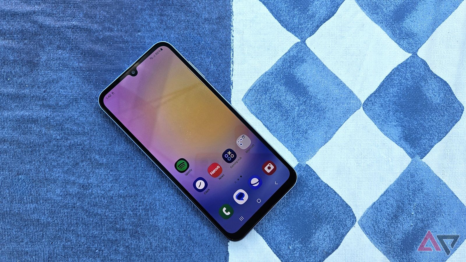 Samsung Galaxy A25 5G deitado em uma superfície plana com padrão azul e tela inicial