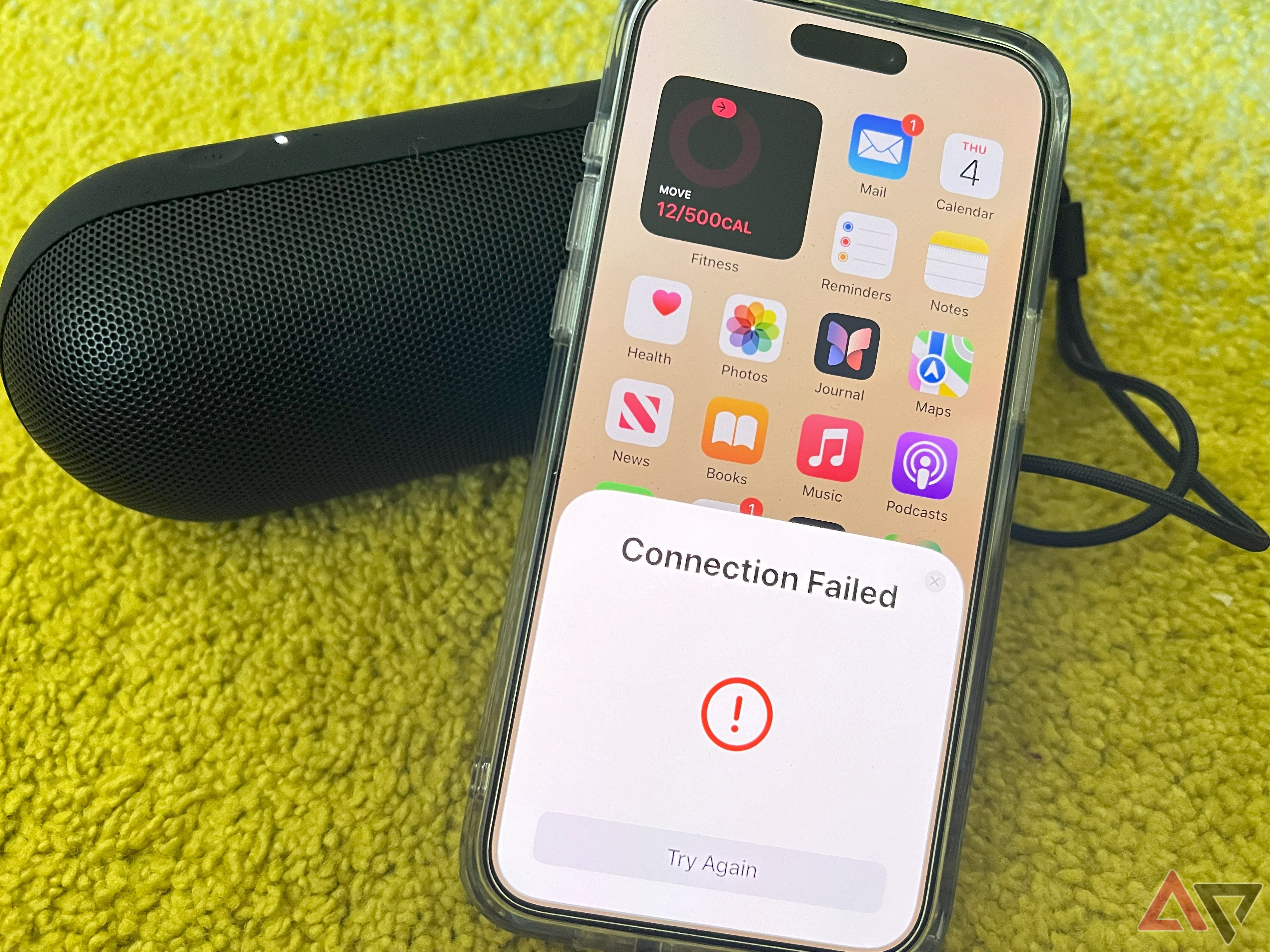 Um iPhone mostrando um aviso de falha de conexão enquanto está apoiado em uma pílula Beats 2024 preta em um tapete verde.