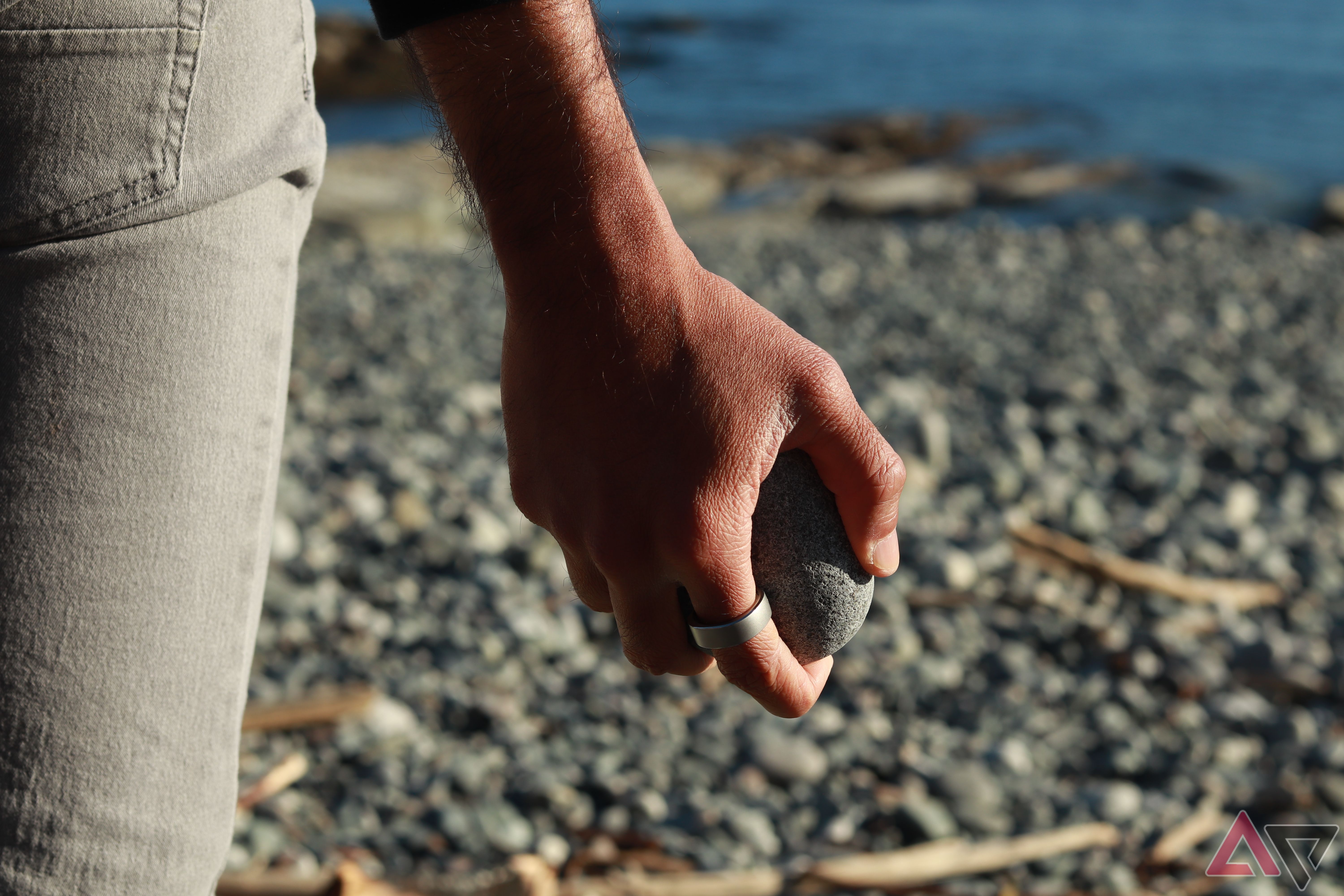 Segurando uma pedra na praia com um anel inteligente no dedo