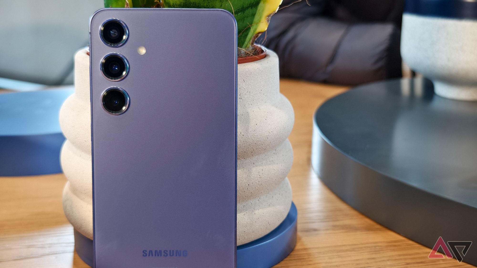 Samsung Galaxy S24+ com acabamento roxo, mostrado apoiado em um vaso de planta