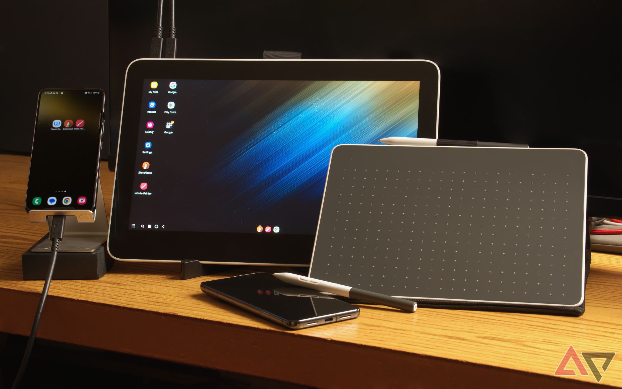 Tablets de desenho da Wacom apoiados em uma mesa ao lado de telefones, um deles mostra o Samsung DeX