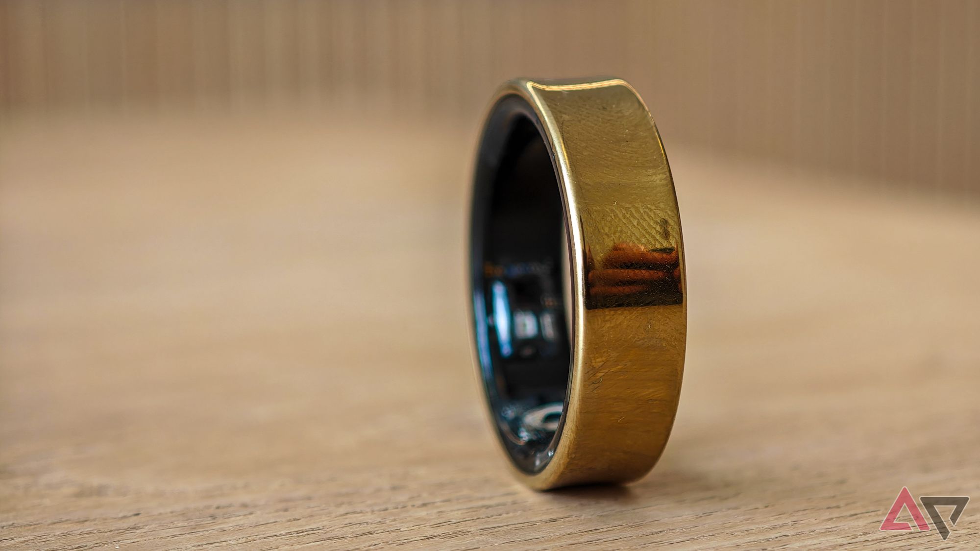 Um Samsung Galaxy Ring dourado deitado de lado sobre uma mesa de madeira clara