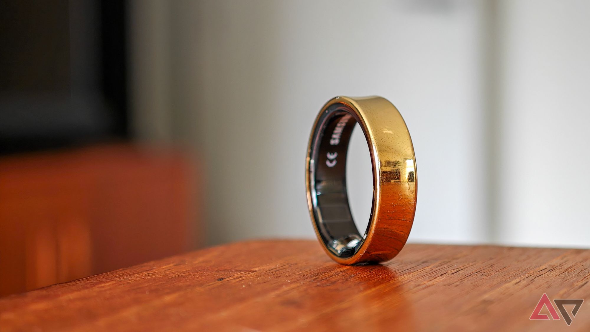 Um Samsung Galaxy Ring dourado apoiado verticalmente na borda de uma mesa de madeira