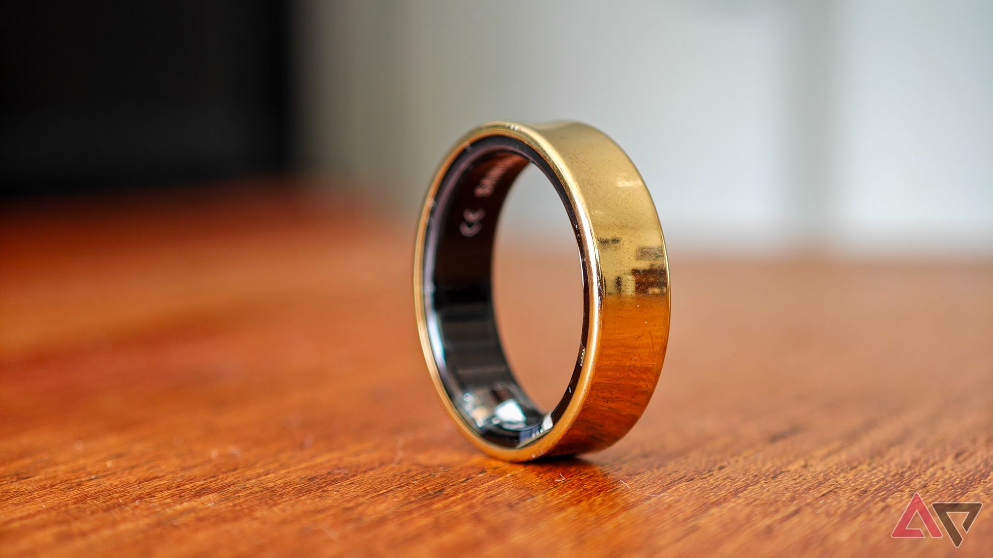 Um Samsung Galaxy Ring dourado apoiado verticalmente sobre uma mesa de madeira