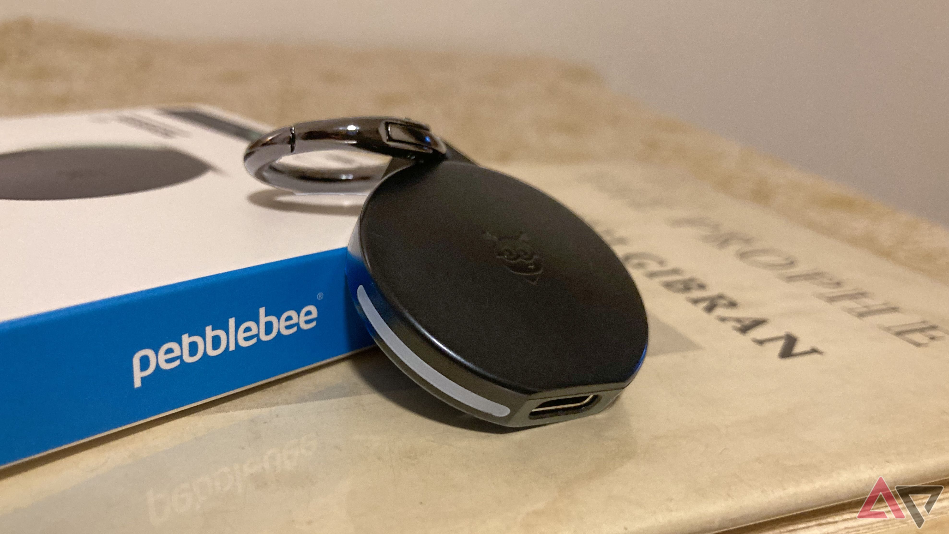 O Pebblebee Clip para Android encostado em sua caixa enquanto está sentado em cima de um livro