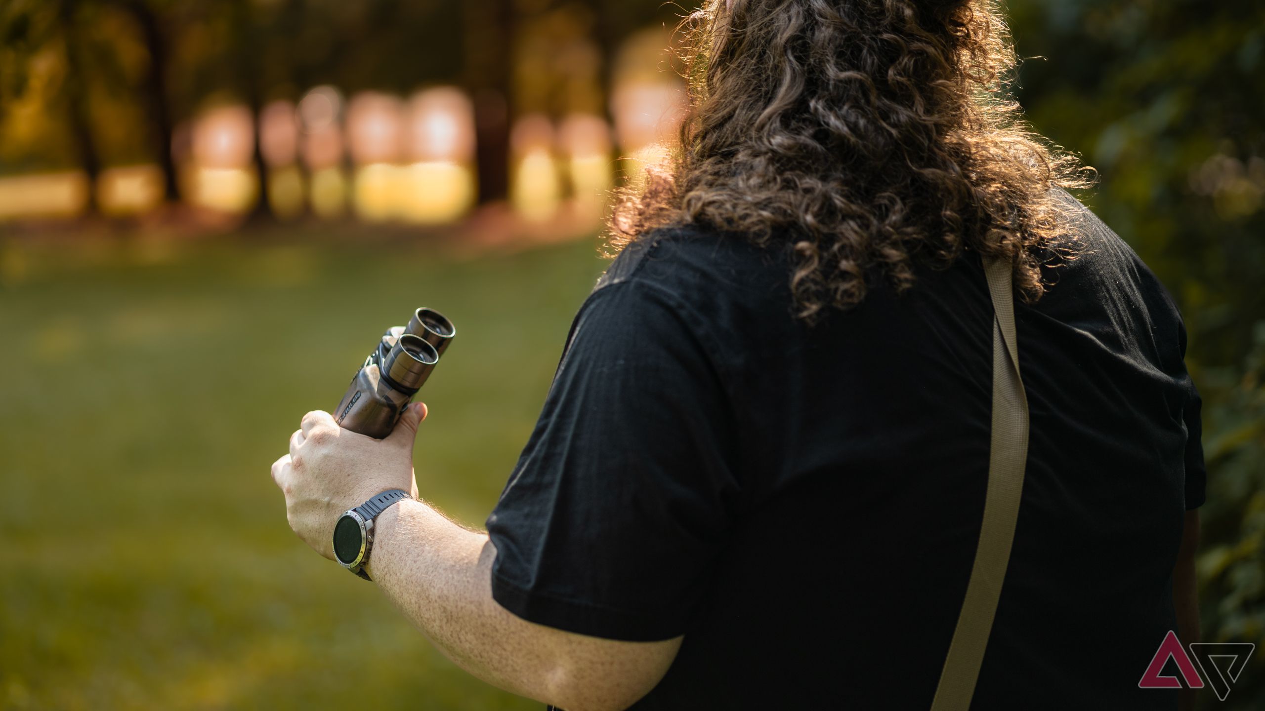 Vista traseira de um homem olhando para o pôr do sol enquanto usa o smartwatch Polar Grit X2 Pro e binóculos