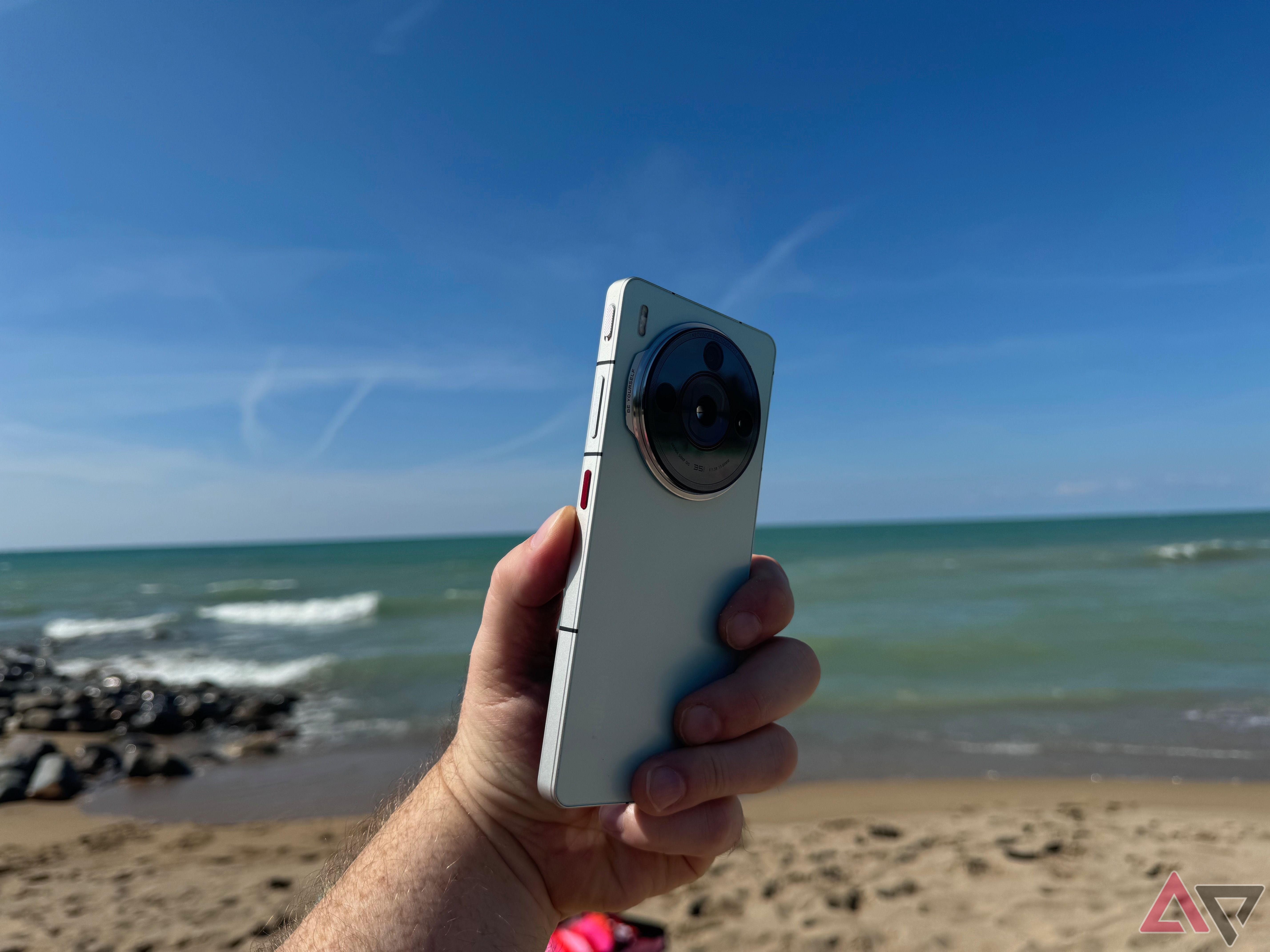 Uma mão segurando um Nubia Z60S Pro verde com uma praia ao fundo.