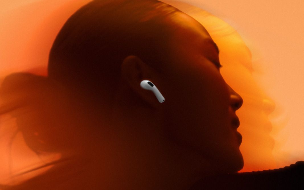 Uma mulher usando AirPods sobre um fundo laranja.