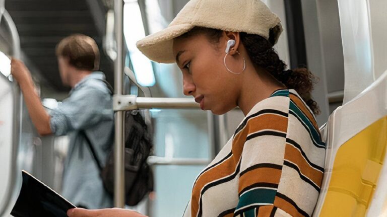 JBL Vibe Beam earbuds product shot showing lady sitting on subway listening to her earbuds