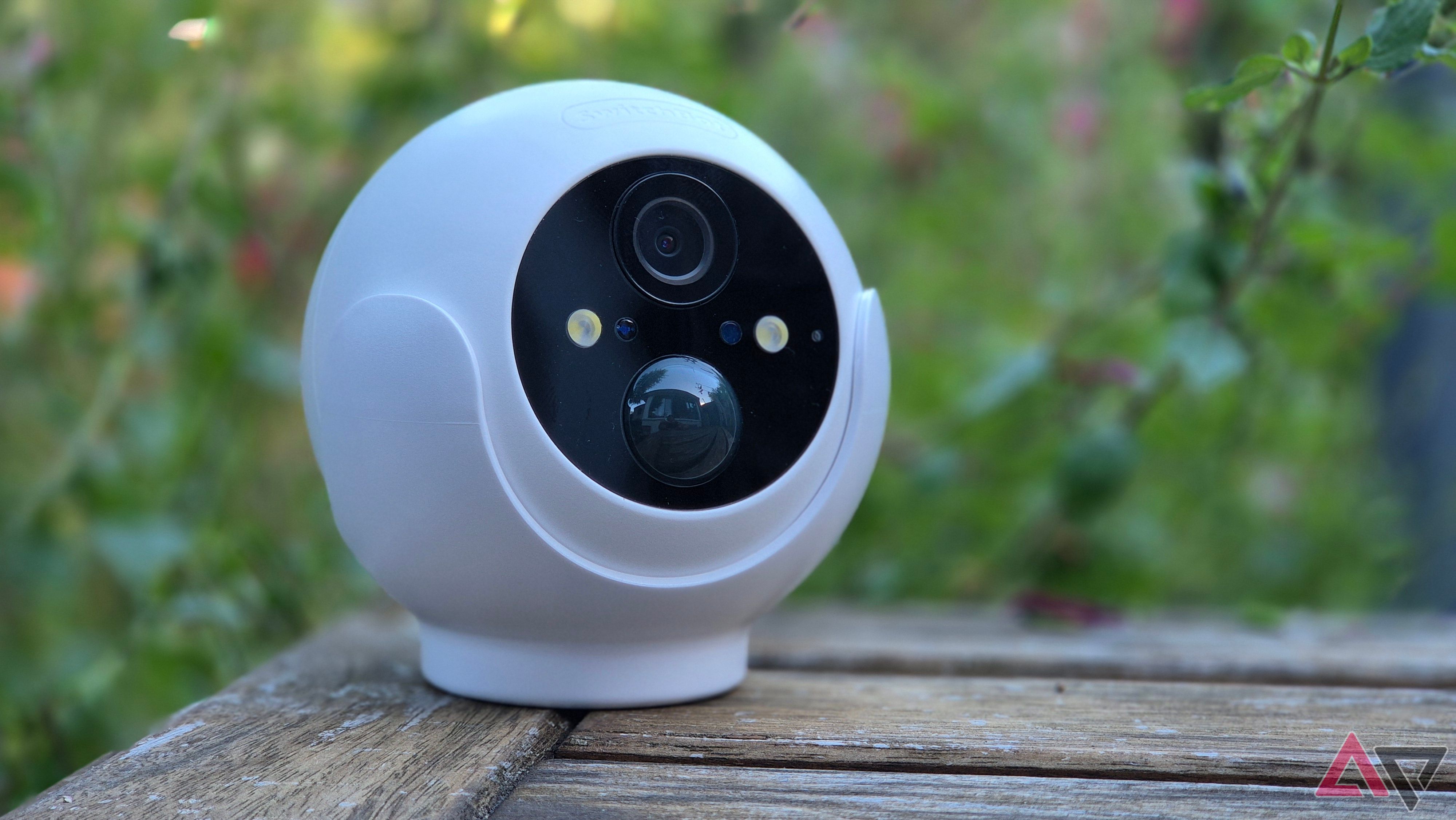 SwitchBot Outdoor Security Cam 2K em uma mesa com plantas ao fundo