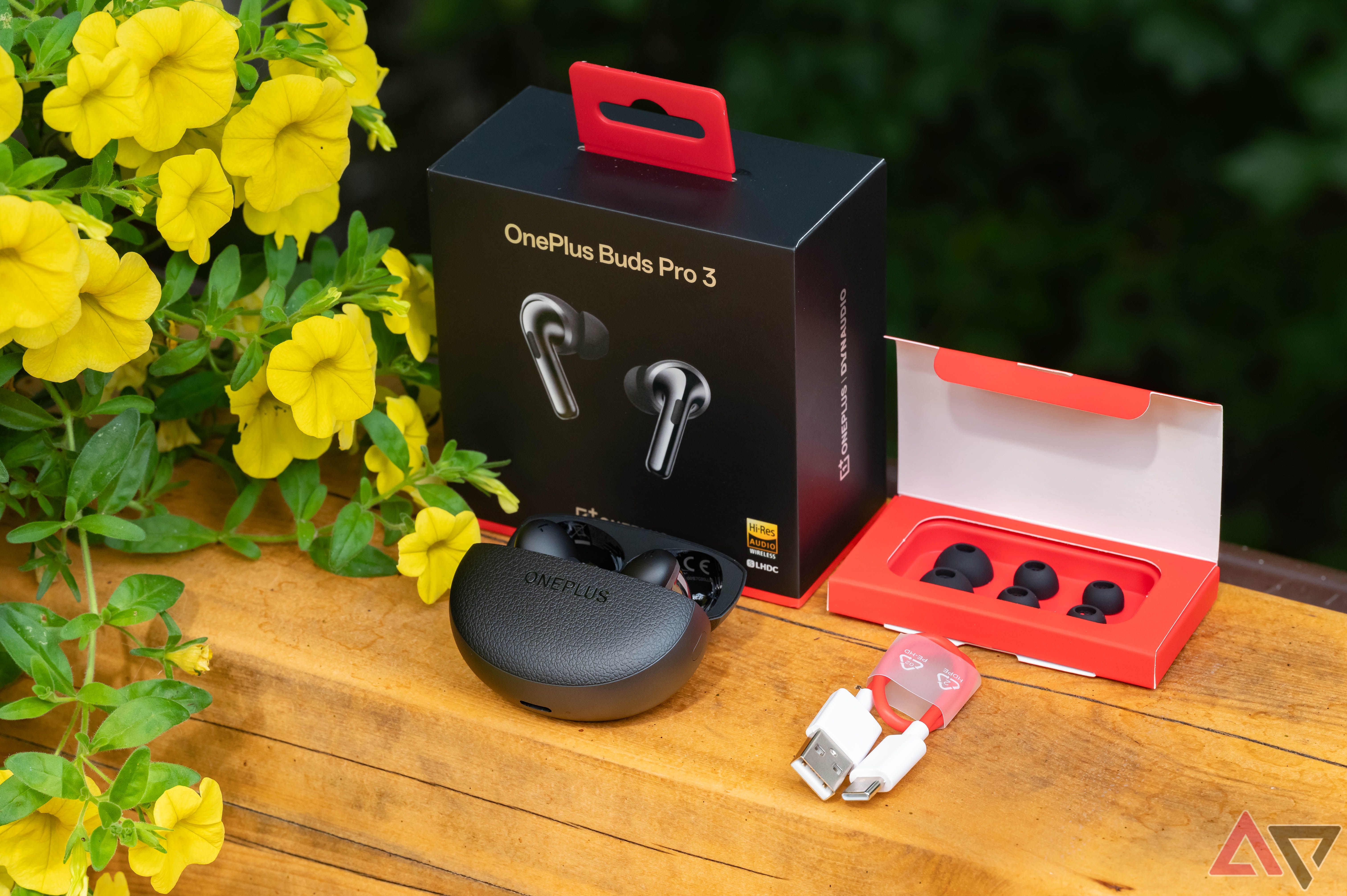 OnePlus Buds Pro 3 com caixa e acessórios ao lado de flores