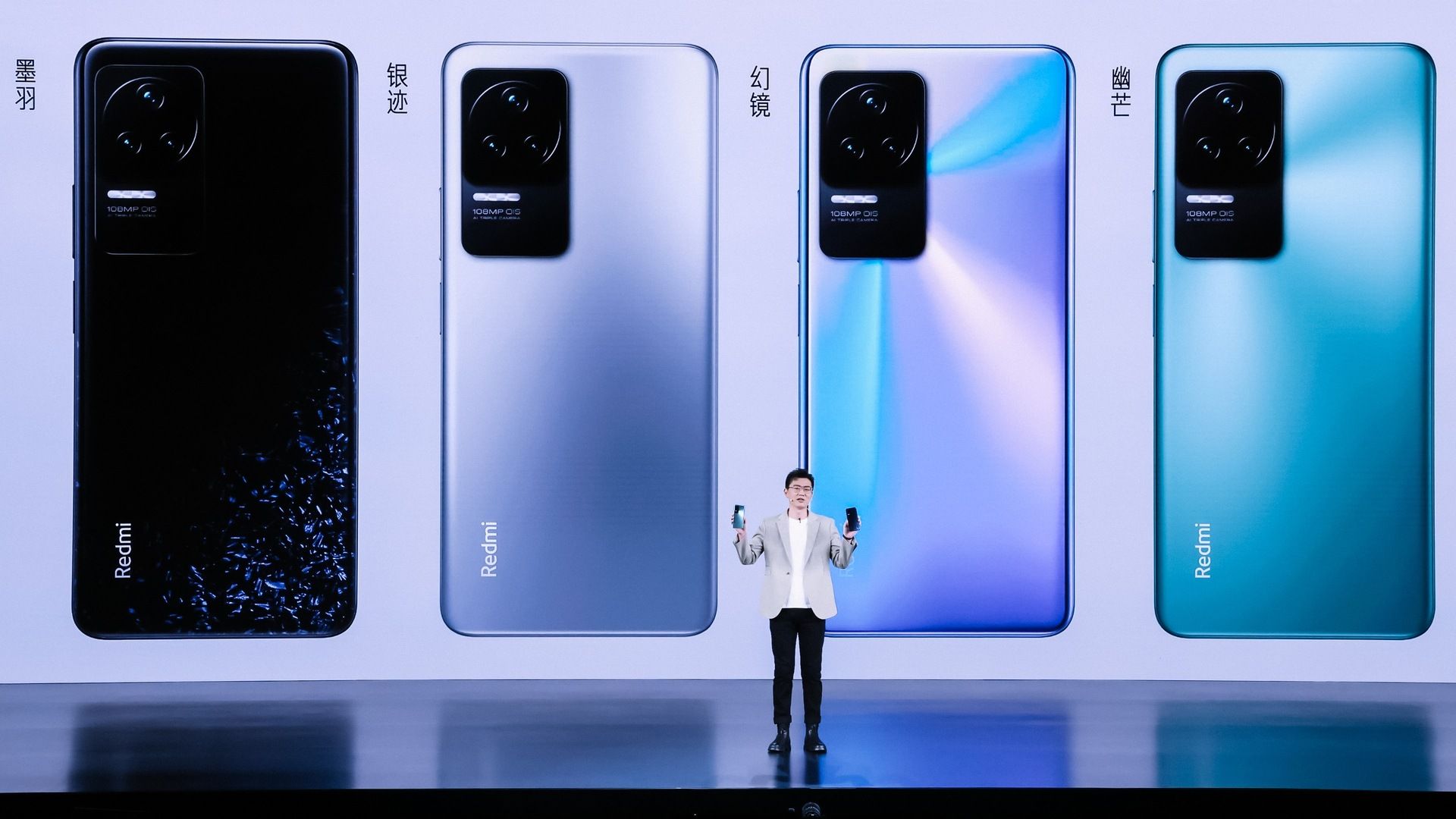 Um executivo da Xiaomi em frente a quatro renderizações do chão ao teto do Redmi K50 Pro