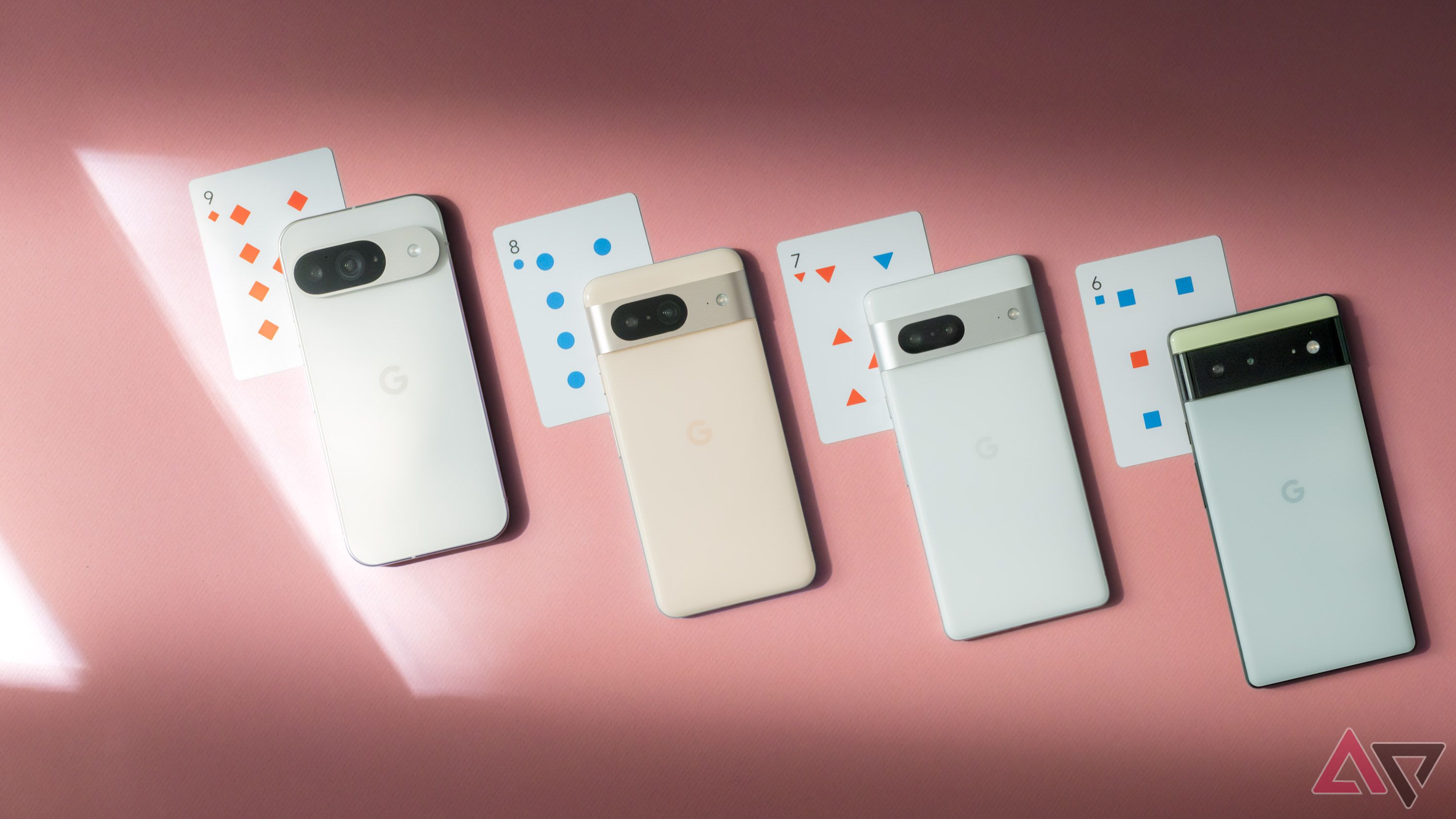 Quatro telefones Google Pixel dispostos em uma superfície rosa ao lado de cartas de baralho